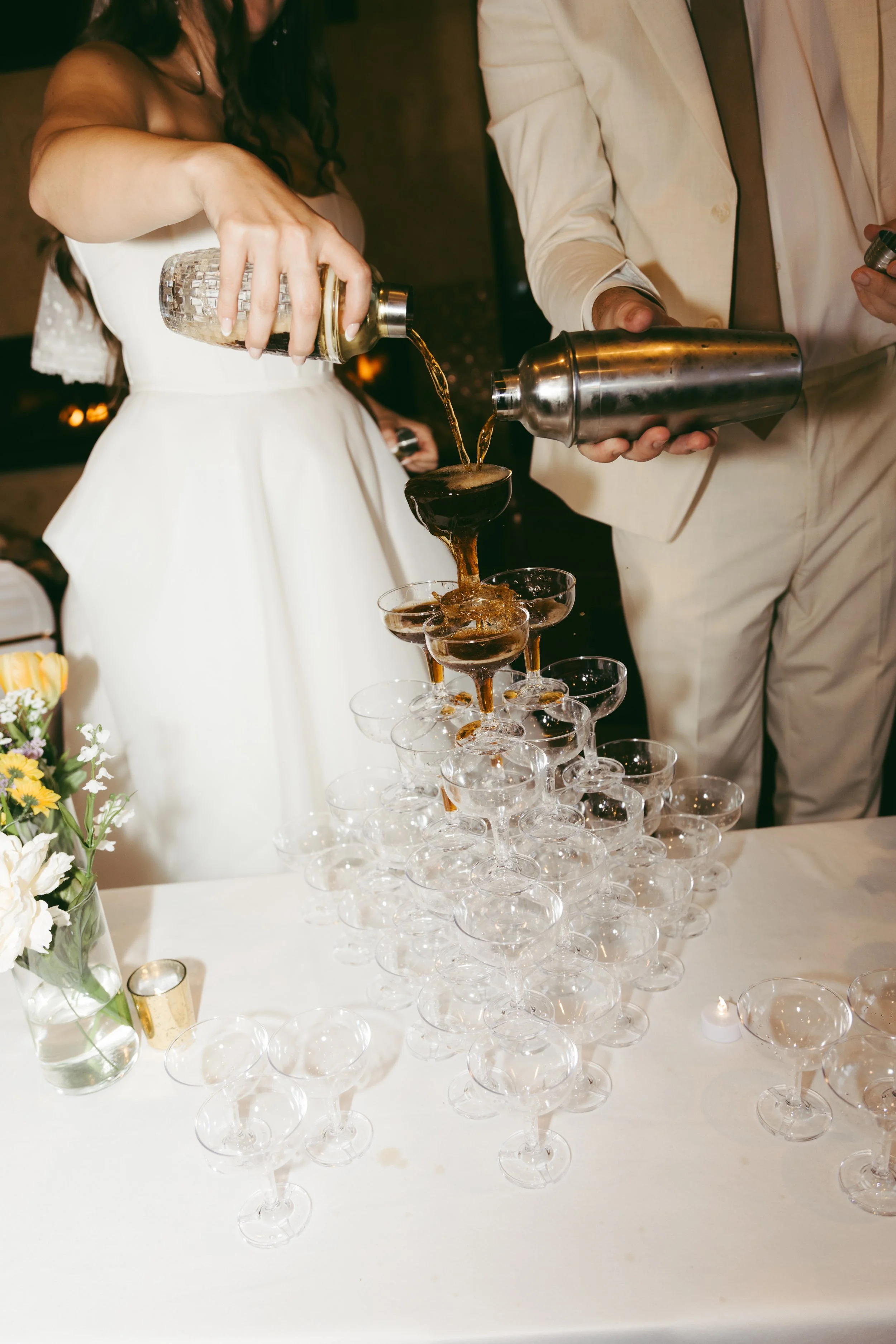 A bride and groom pouring champagne into glasses at a wedding reception.