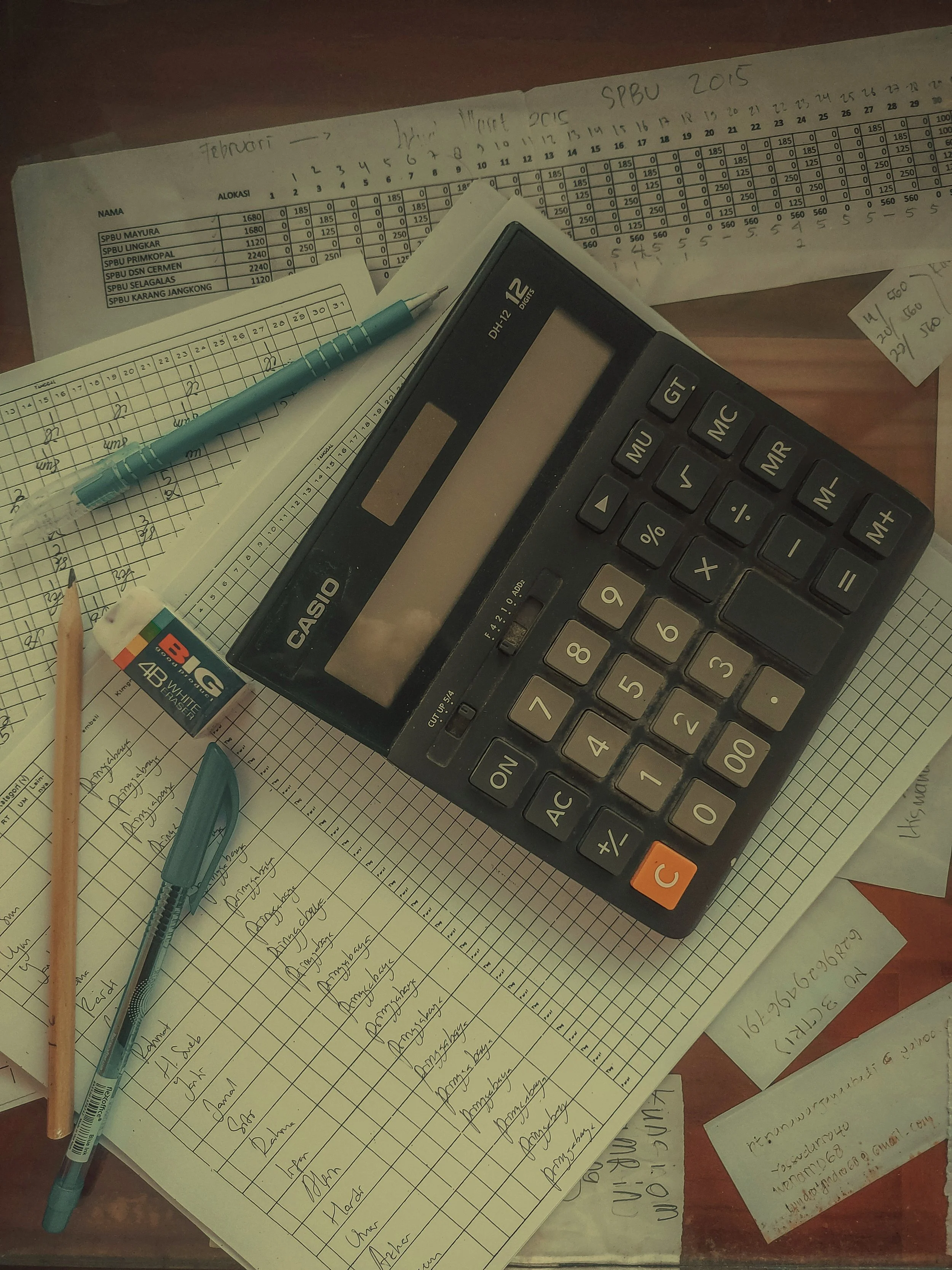 A workspace with papers, a calculator, pens, an eraser, a pencil, and handwritten notes on a wooden desk.