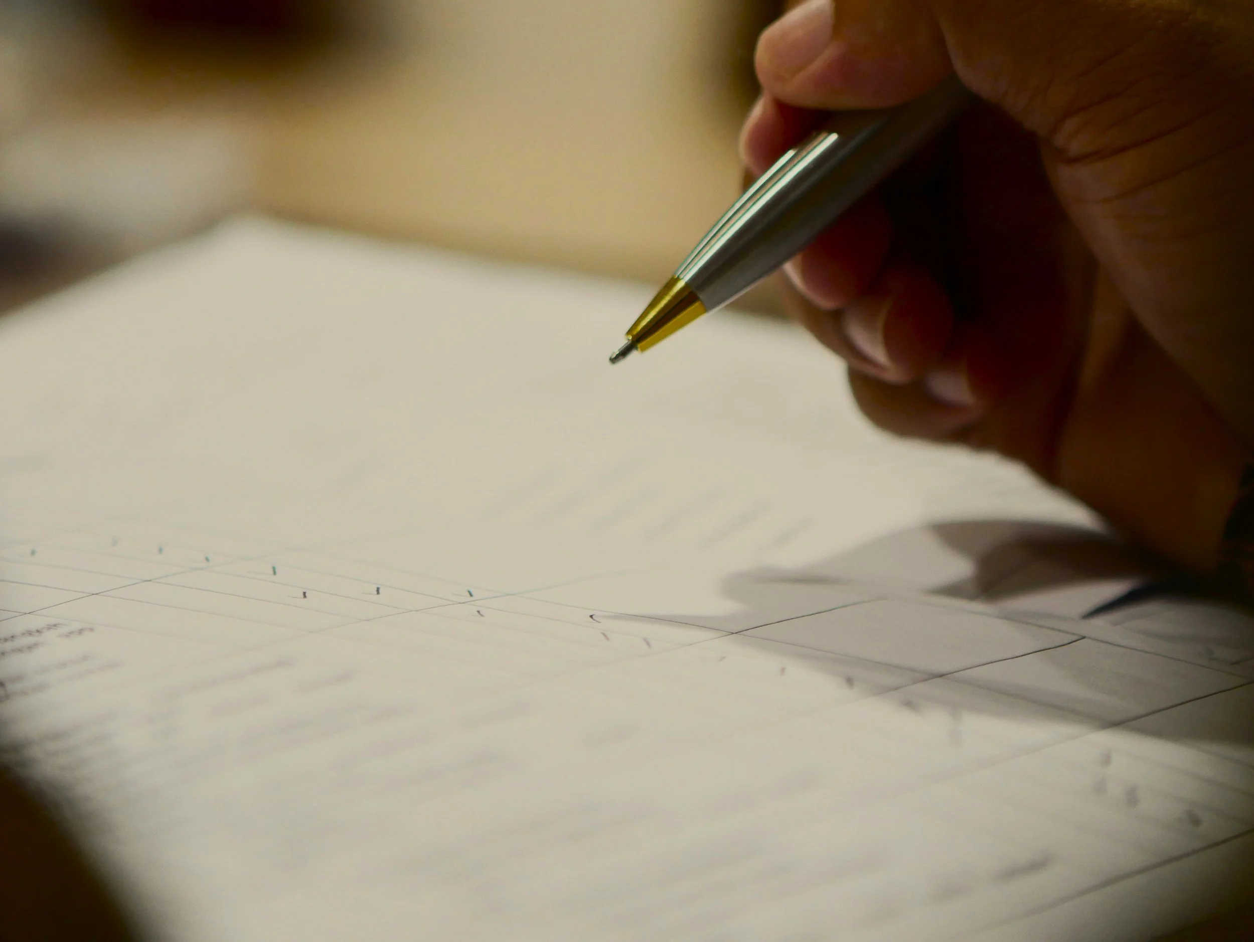 A person’s hand holding a silver and gold pen writing in a notebook with lined pages.