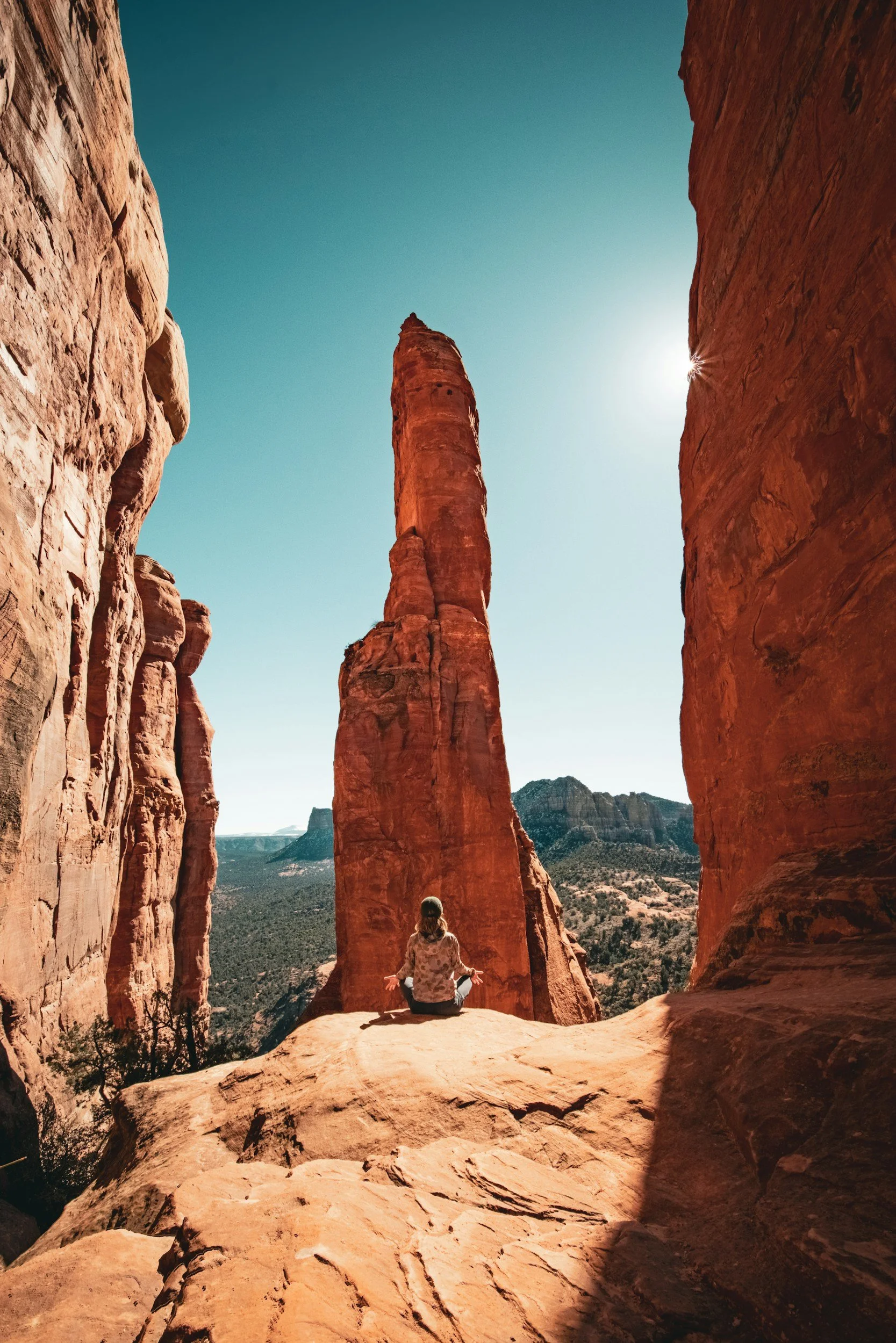 A woman reconnecting with herself sitting on a rock in the desert, surrounded by tall red sandstone rock formations, with a view of a distant mountain and clear sky.