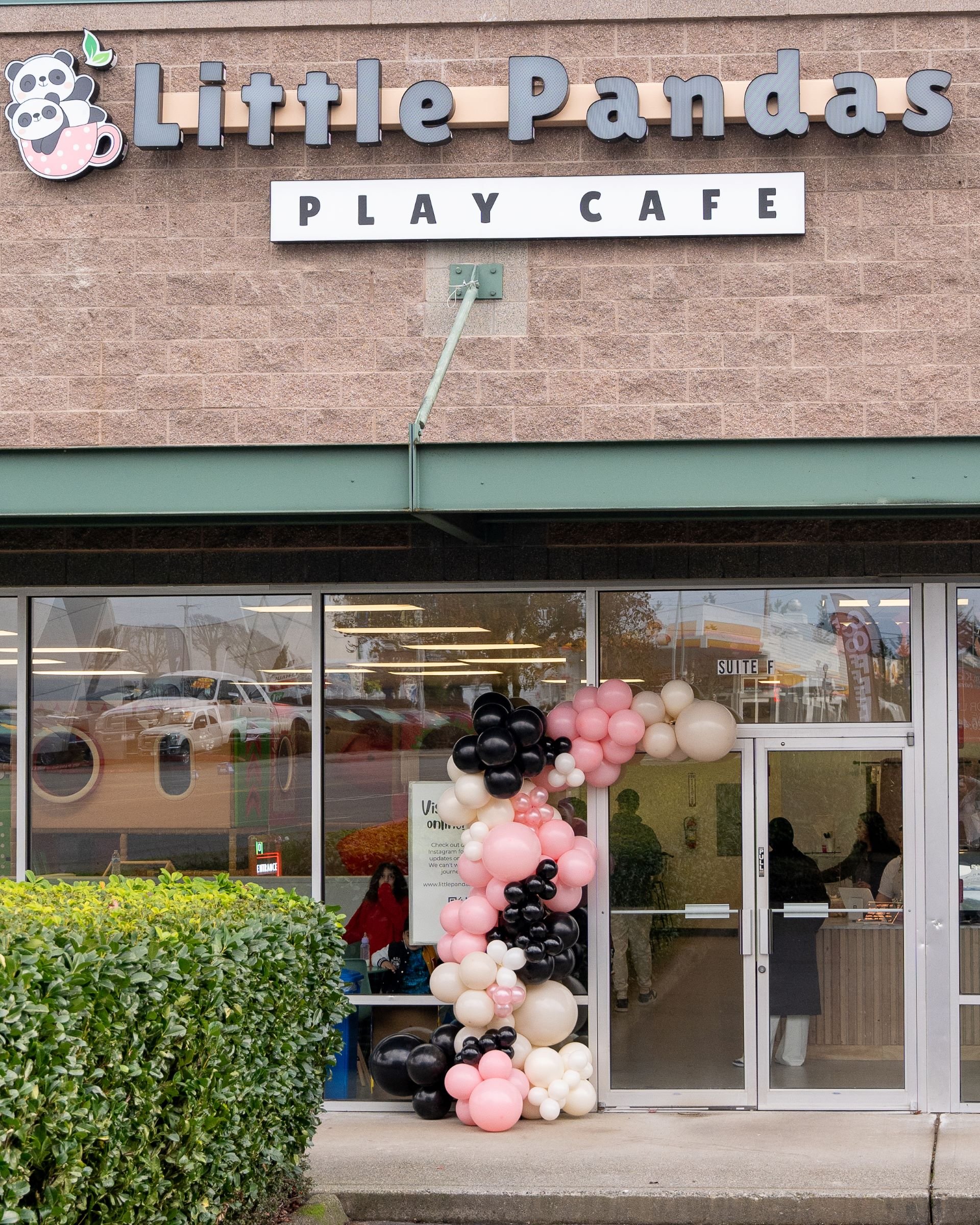 The front of a Little Pandas Play Cafe decorated with pink, white, and black balloons near the entrance.