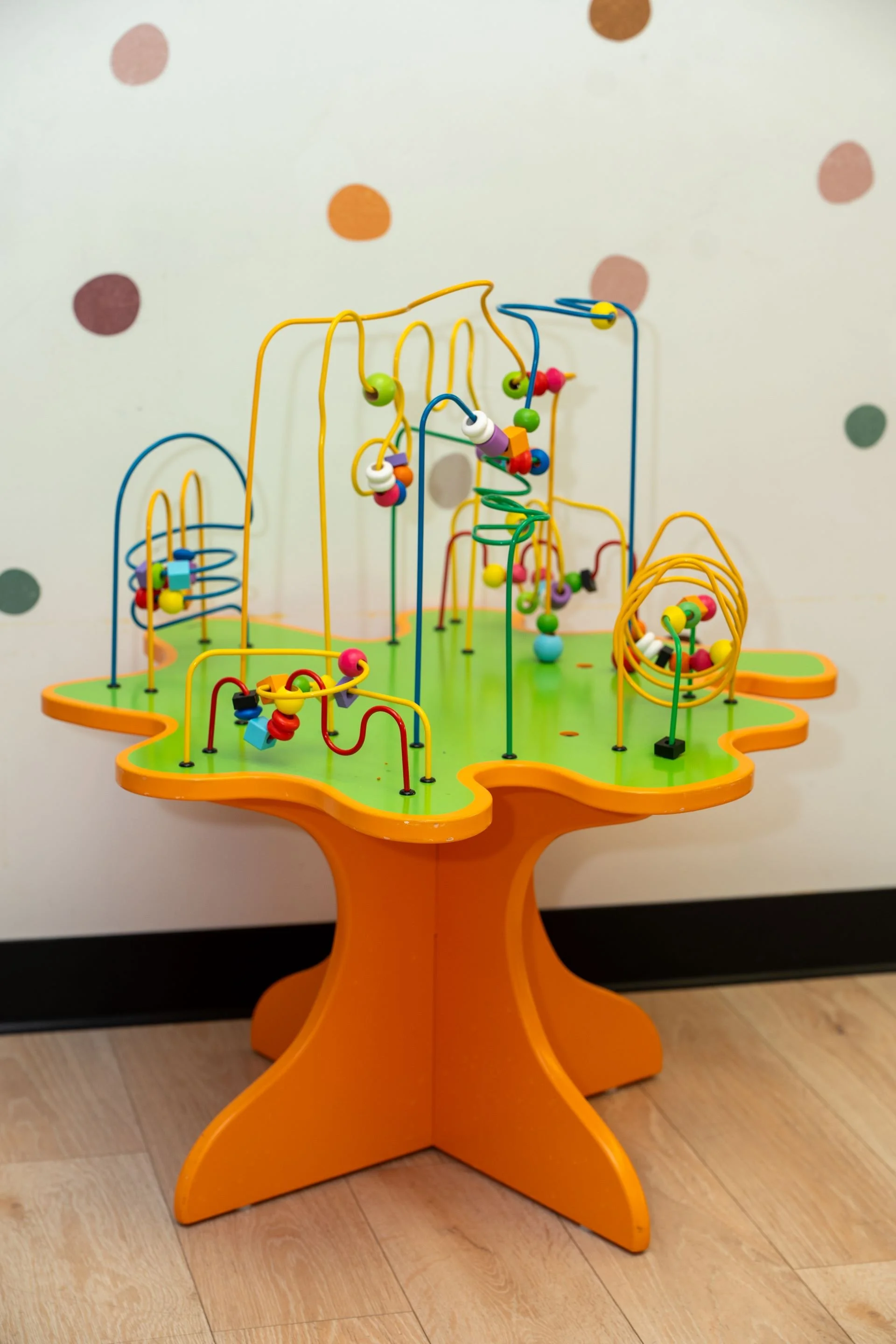Colorful bead maze toy on orange base against a white wall with polka dots.