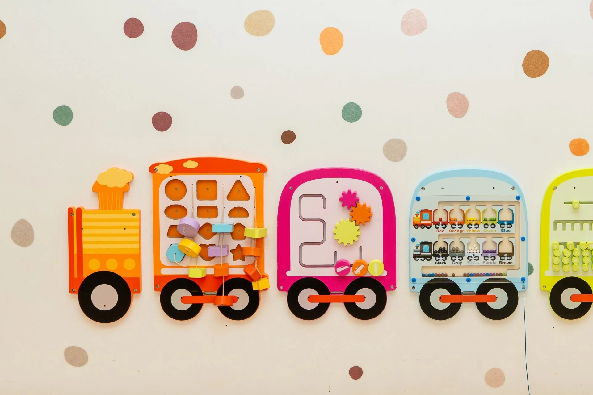 Colorful children's toy train with different shapes and gears, mounted on a white wall with polka dots.