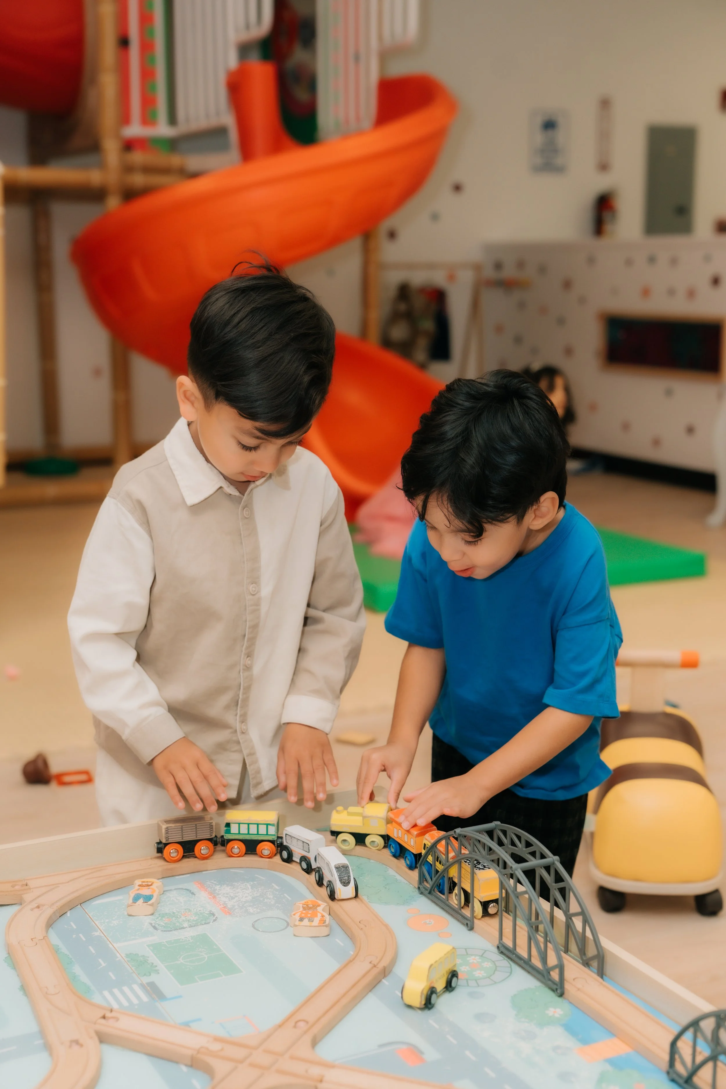 Two boys playing with toy train set on a play table in a children's playroom.
