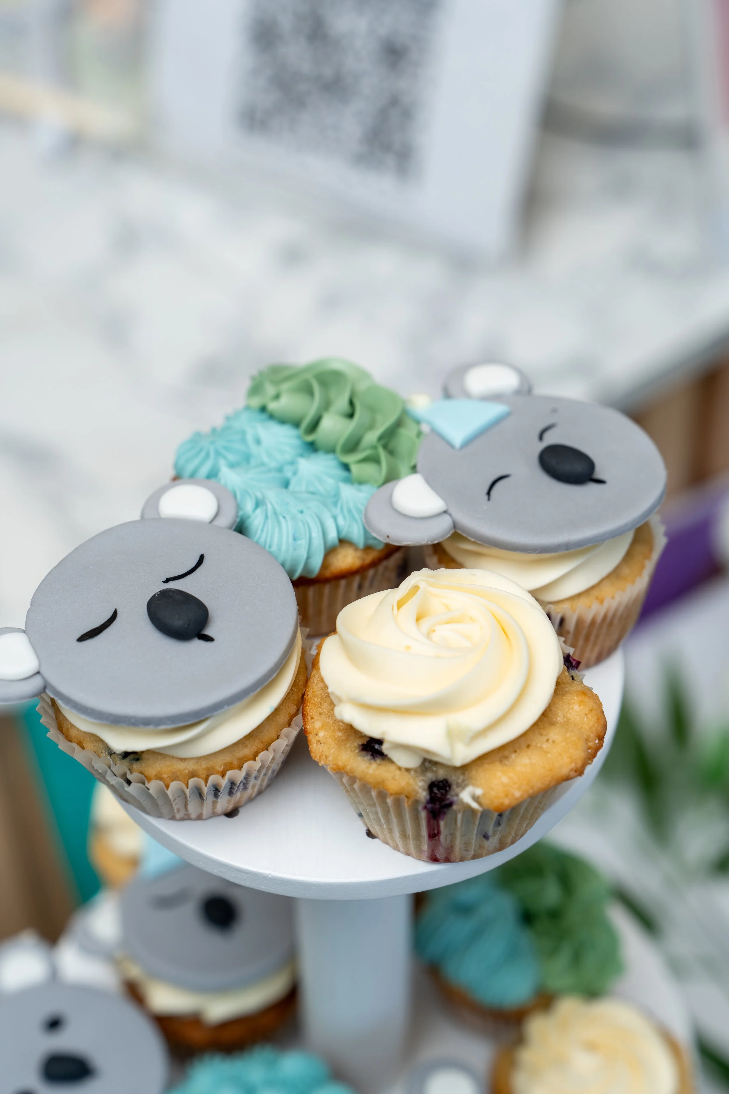 Cupcakes decorated with koala bear faces, green and blue frosting, and one with white swirl frosting.