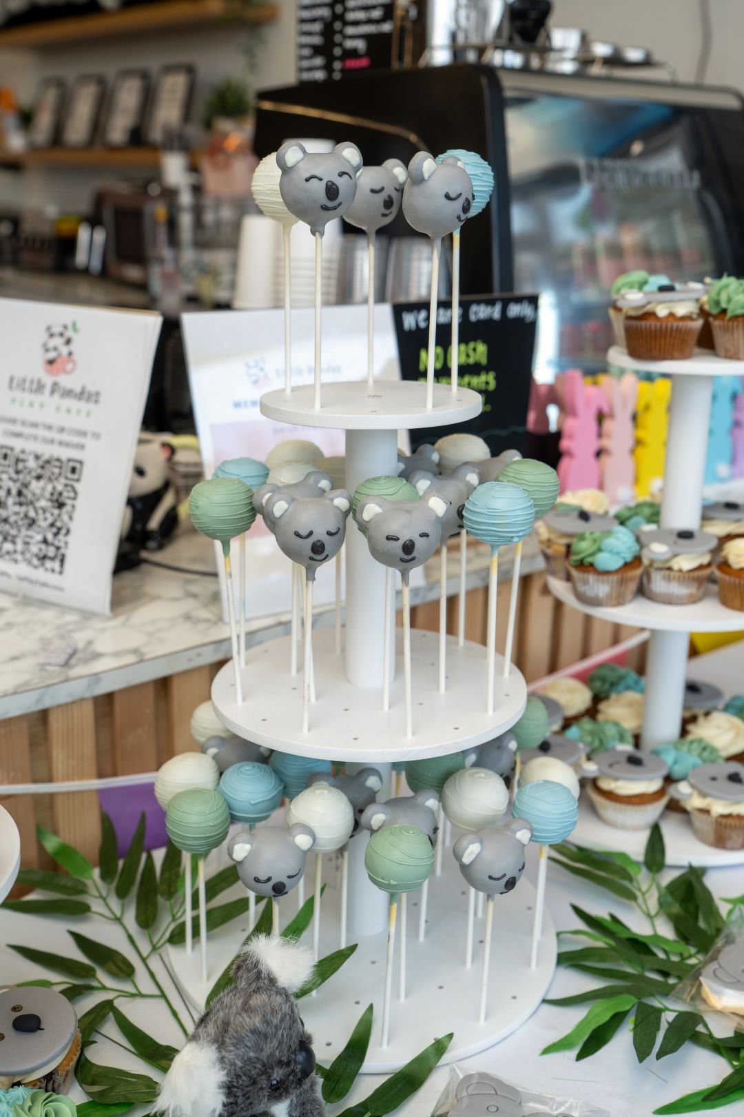 Display of bear-shaped cake pops and spherical treats in pastel colors on a multi-tiered stand in a bakery or cafe setting.