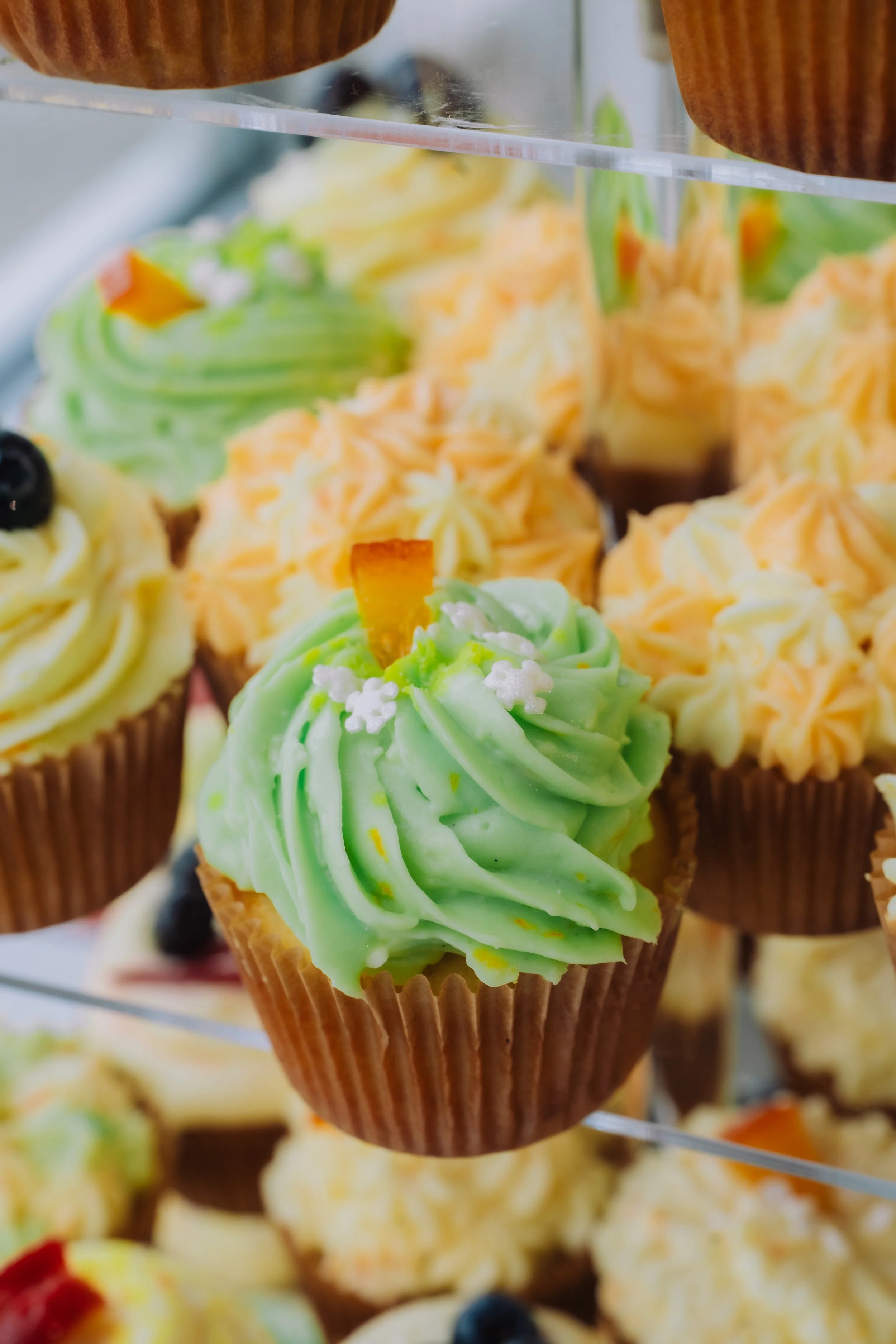 Colorful cupcakes with green, yellow, and orange frosting on display.
