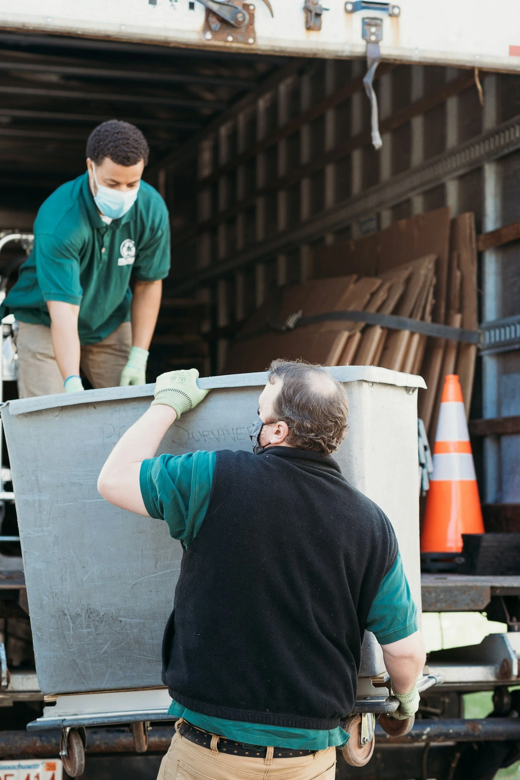 Gloved and masked professionals carrying plastic bin from a truck