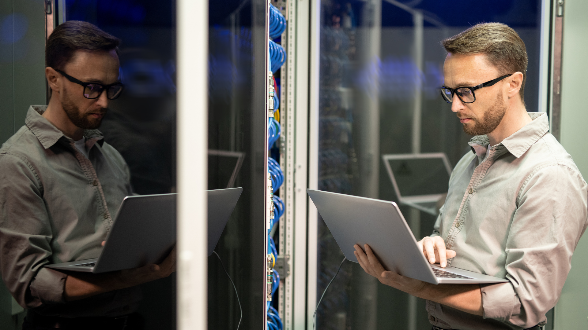 Man with glasses holding silver laptop server room
