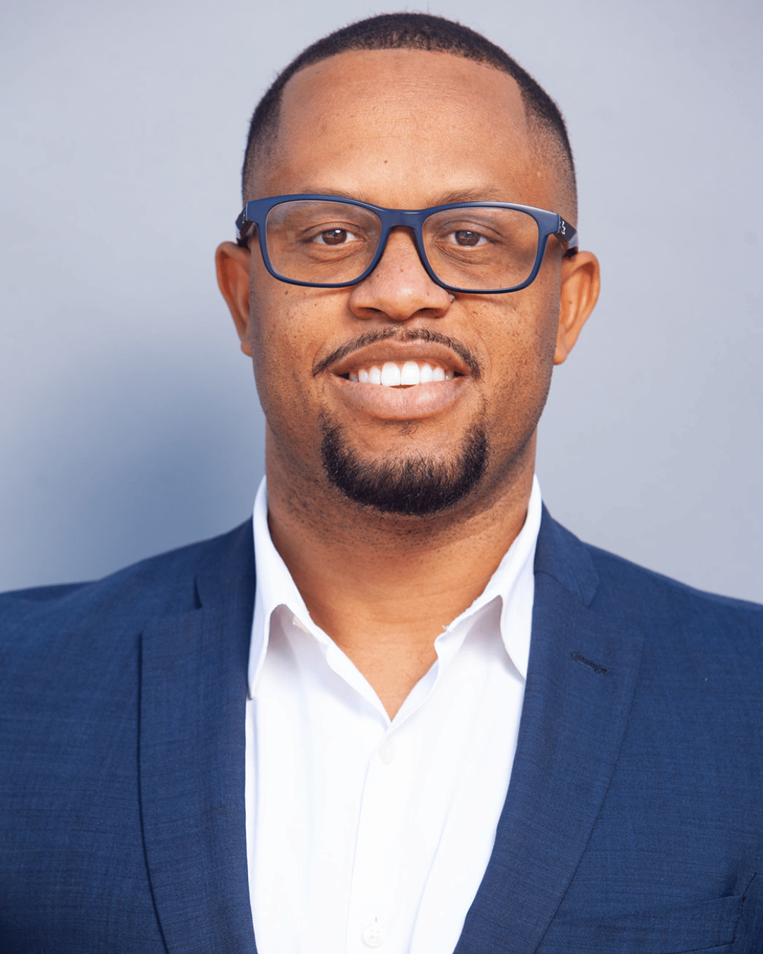 Franz Delima of Arise & Own wearing glasses, a white shirt, and a blue blazer, smiling against a neutral background.