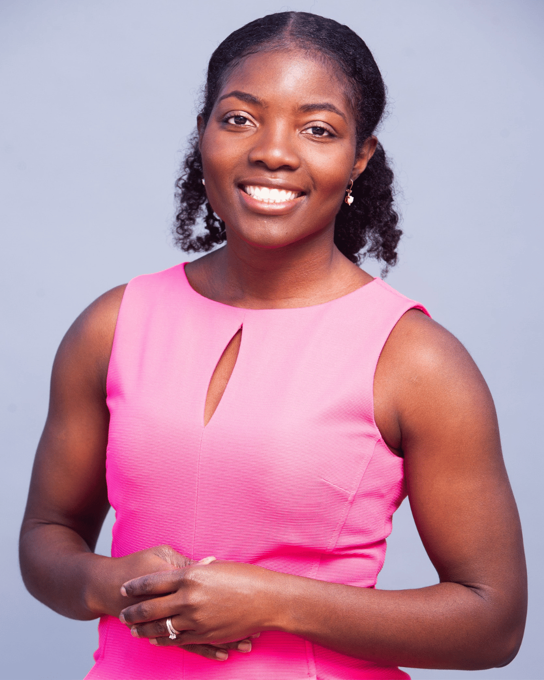 Danielle Delima of Arise & Own wearing a sleeveless pink dress, smiling, standing against a plain grey background.
