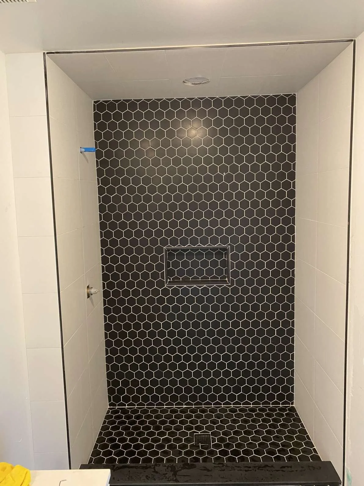 A modern walk-in shower with black hexagonal tile on the back wall and floor, white tiles on the side walls, and a built-in niche in the back wall for toiletries.