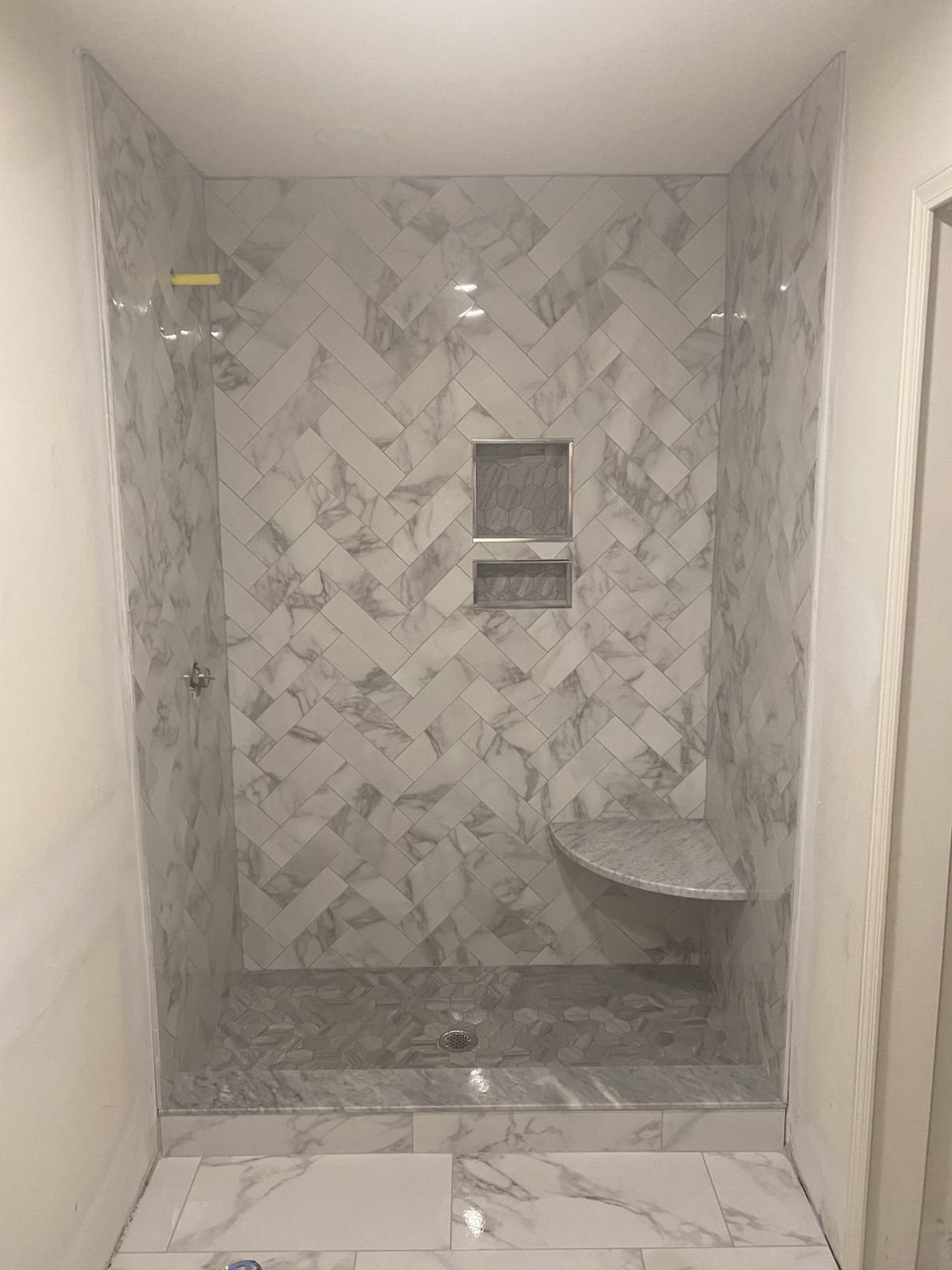 Marble shower with a herringbone tile pattern, built-in shelf, and bench, with white and gray marble tiling.