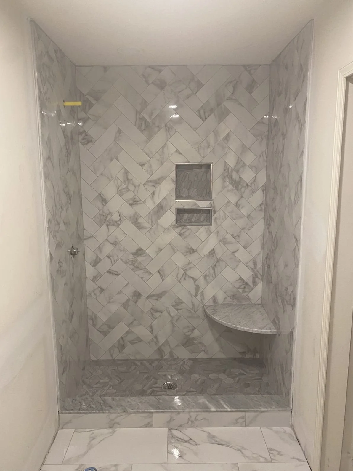 A walk-in shower with gray and white marble tile, a built-in niche, and a curved marble shelf.