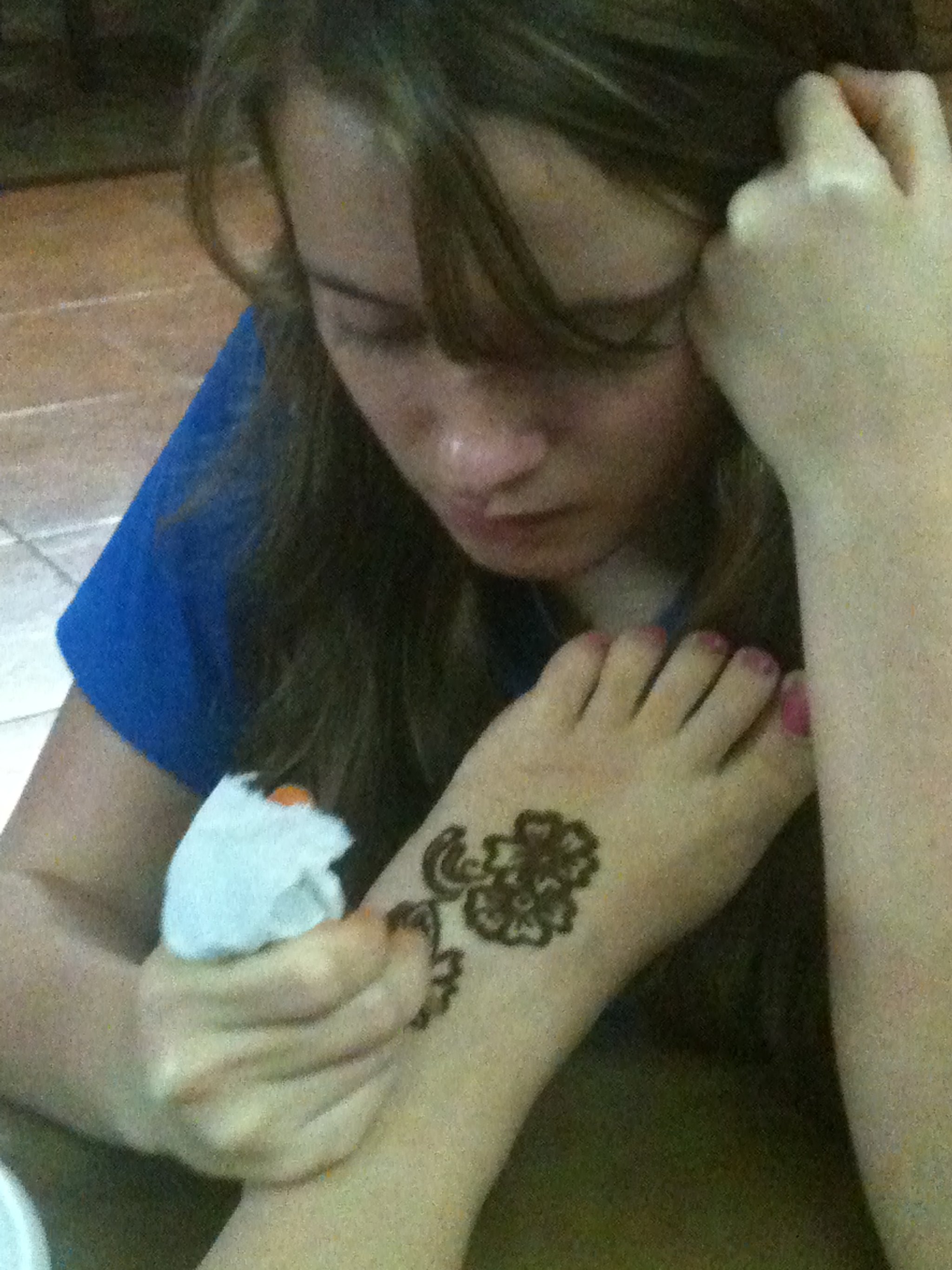 A girl with long dark hair and glasses resting her head on a tattooed arm.