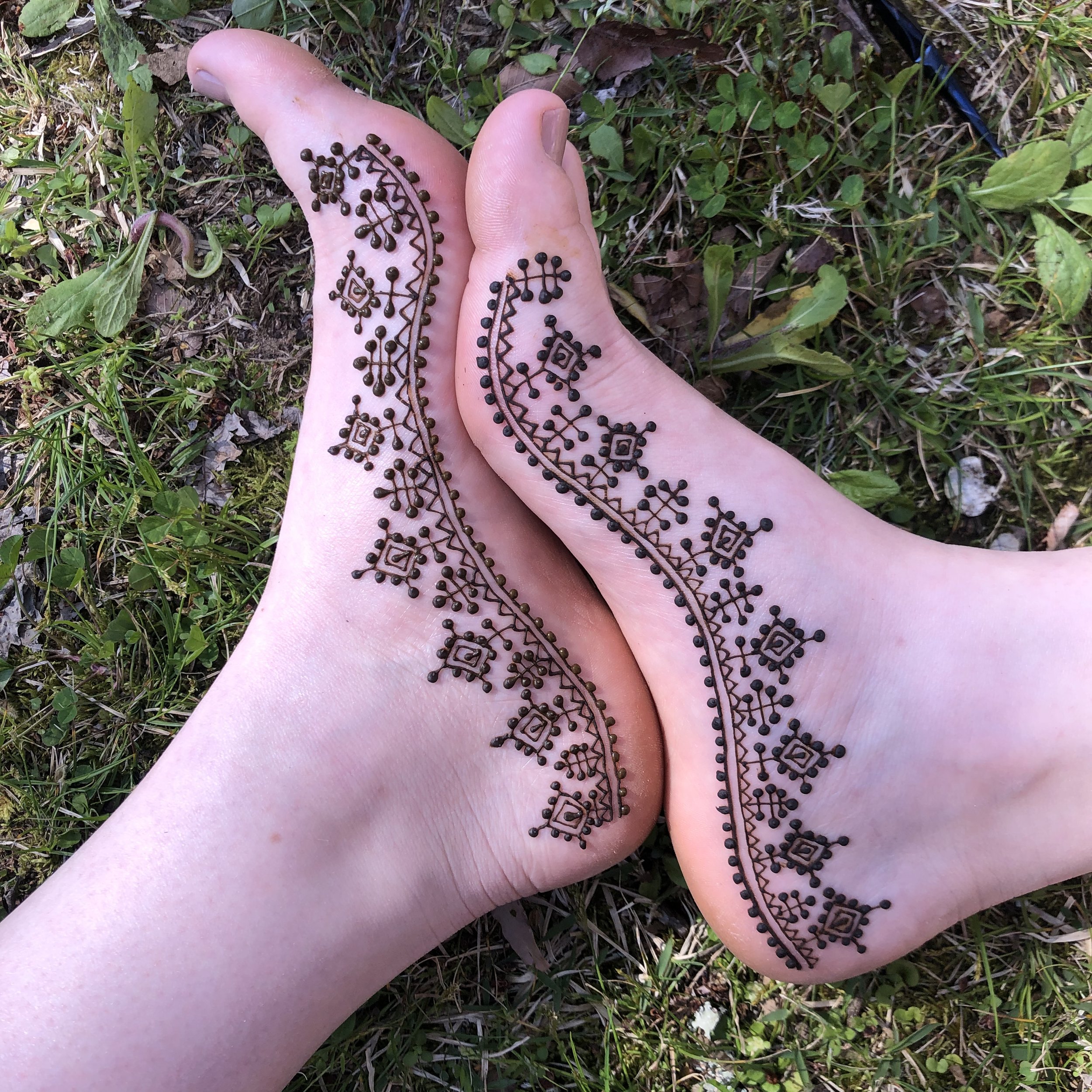A hand with henna tattoo on the palm resting on grass and dirt.
