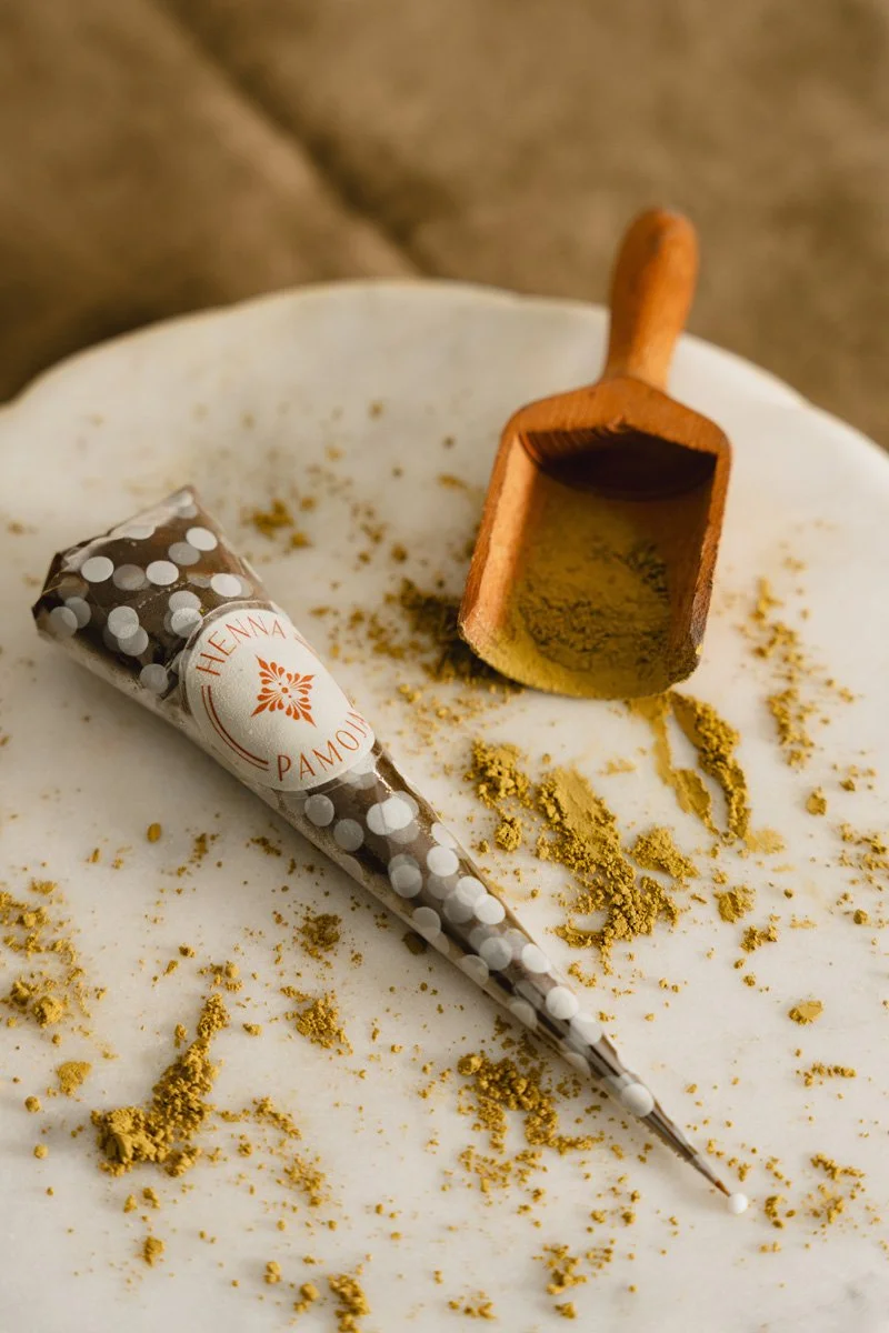Culinary powders, a small wooden scoop with green spice, and a decorated pastry tube with white polka dots on a white surface.