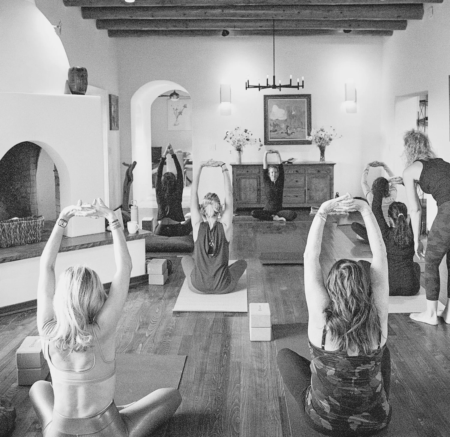 black and white grainy image of group of women doing yoga indoors with a guide at the front