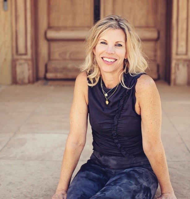 image of Courtney - blonde hair, blue eyes, wearing a black tank top and jeans sitting on concrete steps in front of a wooden door