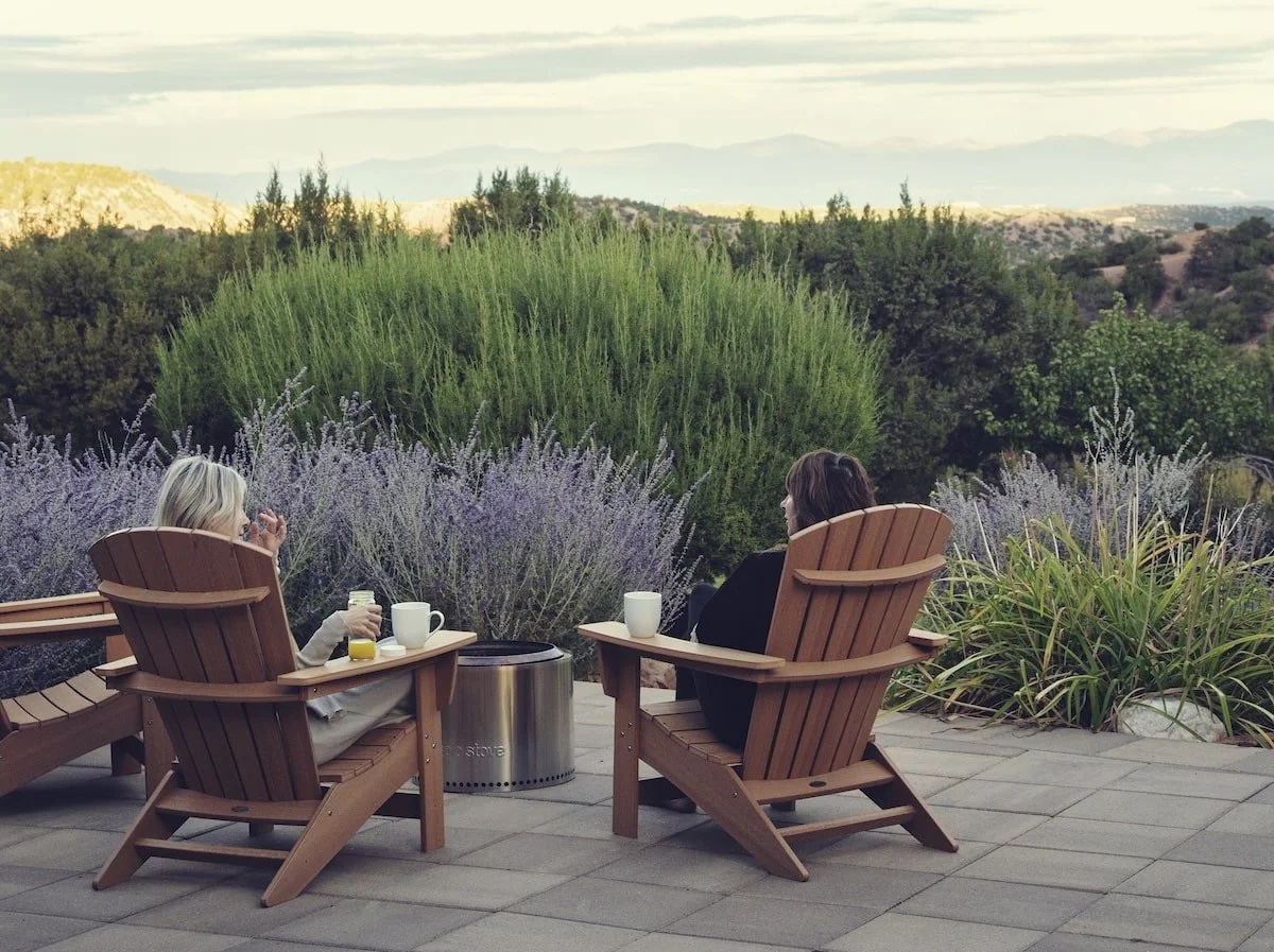 image of two people sitting in chairs in an outdoor garden holding coffee and talking