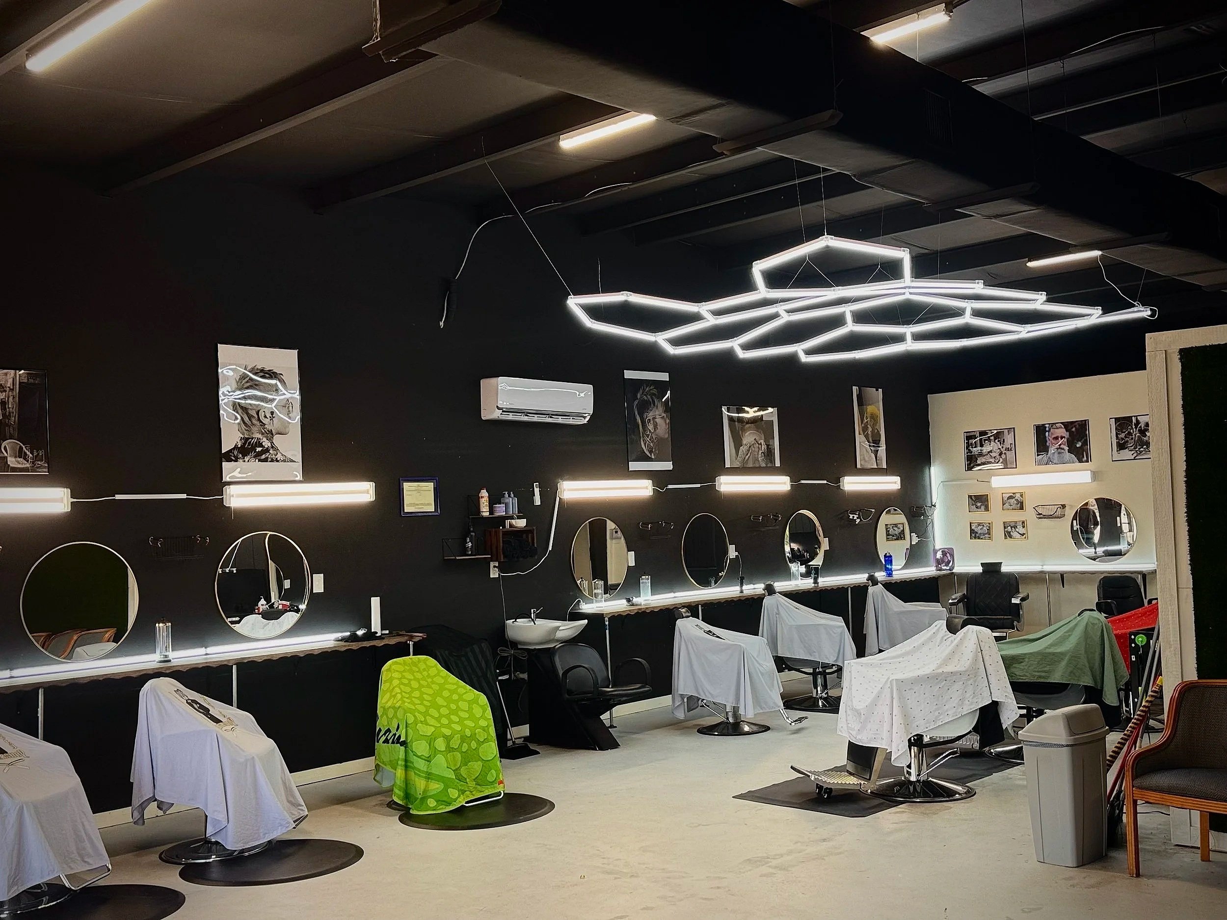 Inside a modern barbershop with multiple barber chairs covered with towels, mirrors on the wall, and contemporary lighting fixtures hanging from the ceiling.