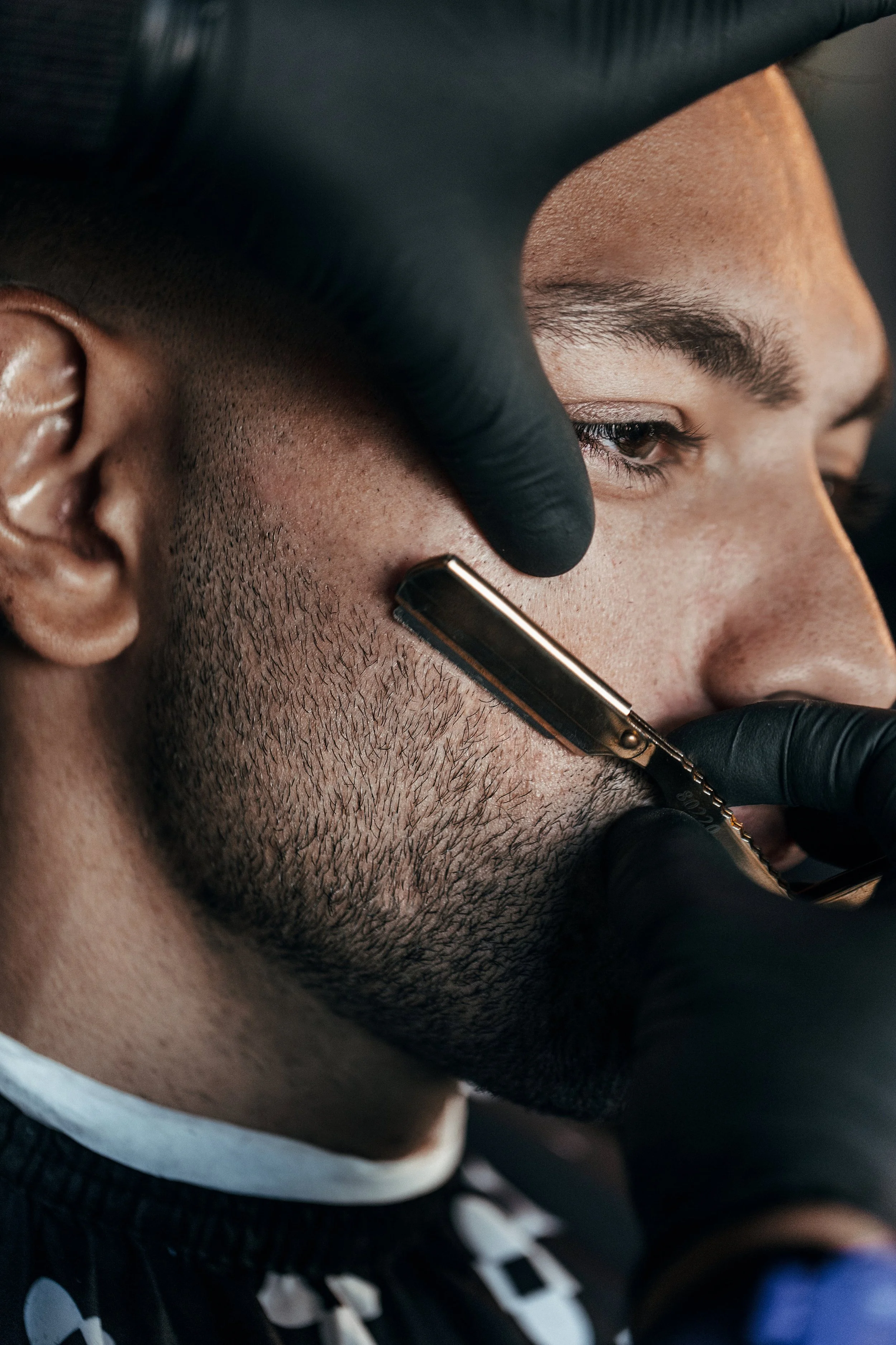 Barber shaving a man's beard with a straight razor in a salon.