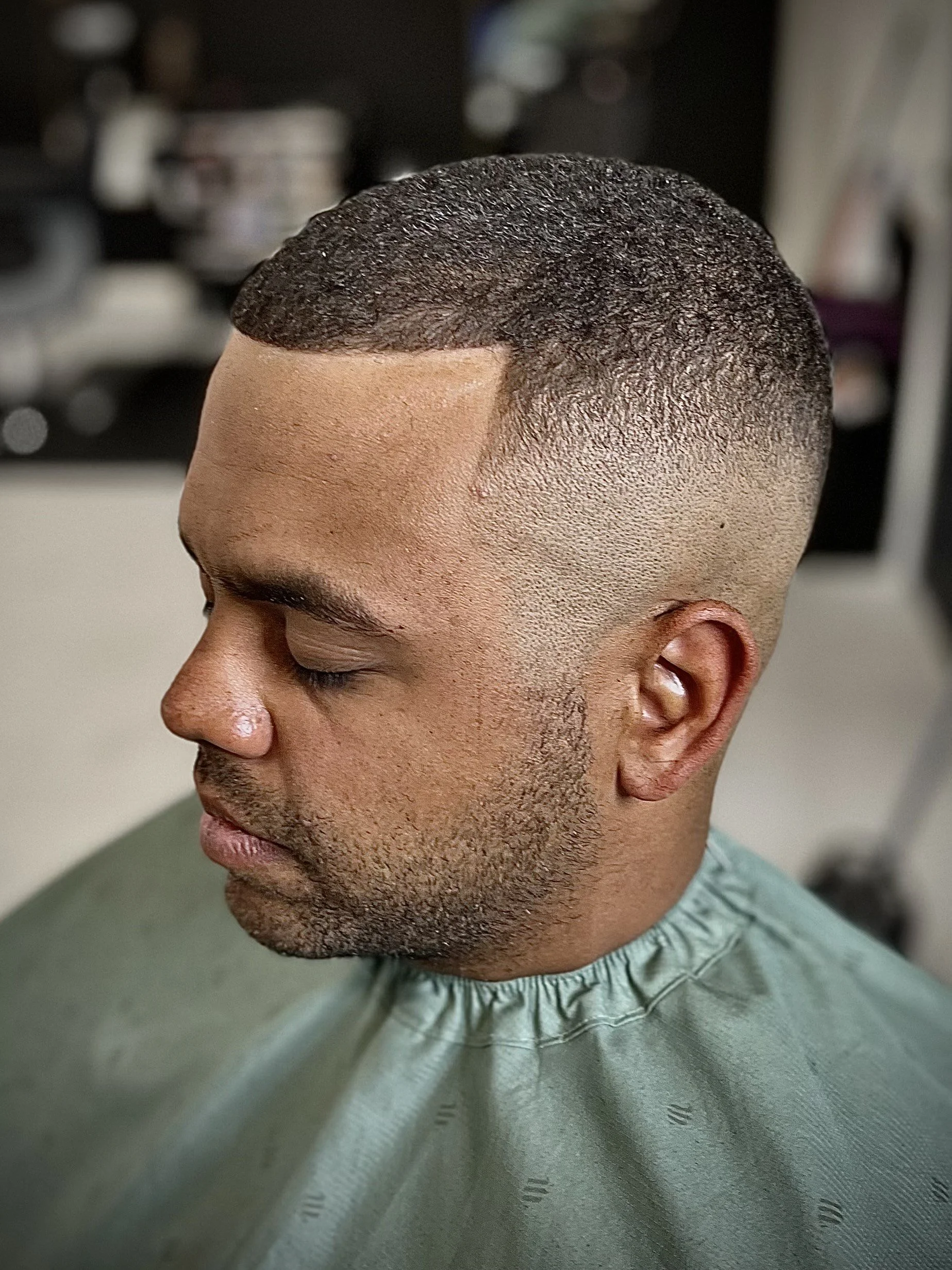A man with a fresh fade haircut sitting in a barbershop chair.