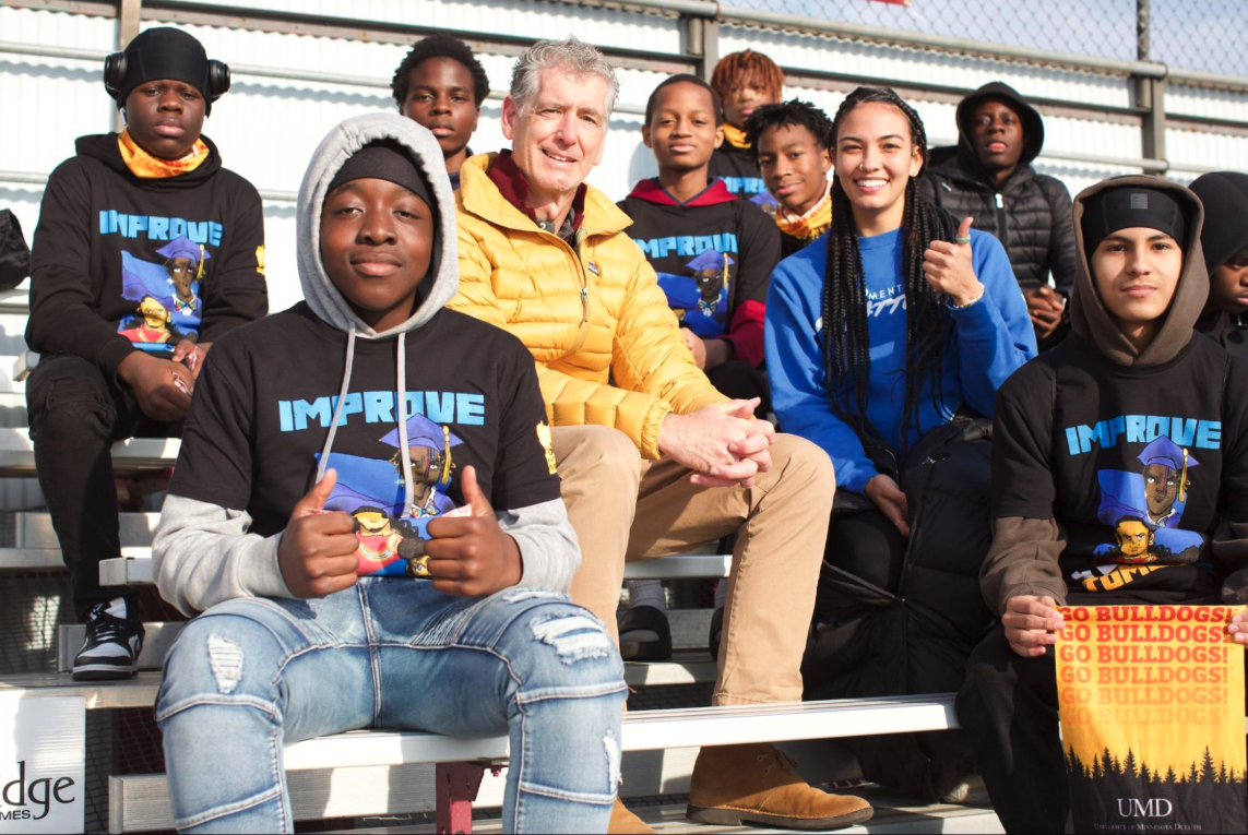 Group of IYT Brothers and a community partner sitting on bleachers.