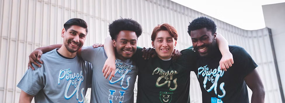 Four young men smiling with their arms around each other's shoulders outside