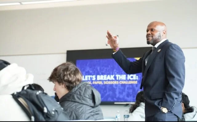 Man in a suit giving a presentation to students in a classroom.
