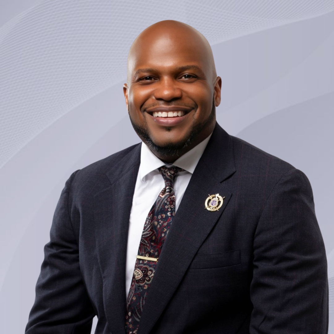 Our Wisconsin ED in a dark suit, white shirt, and paisley tie, posing against a light gray background.