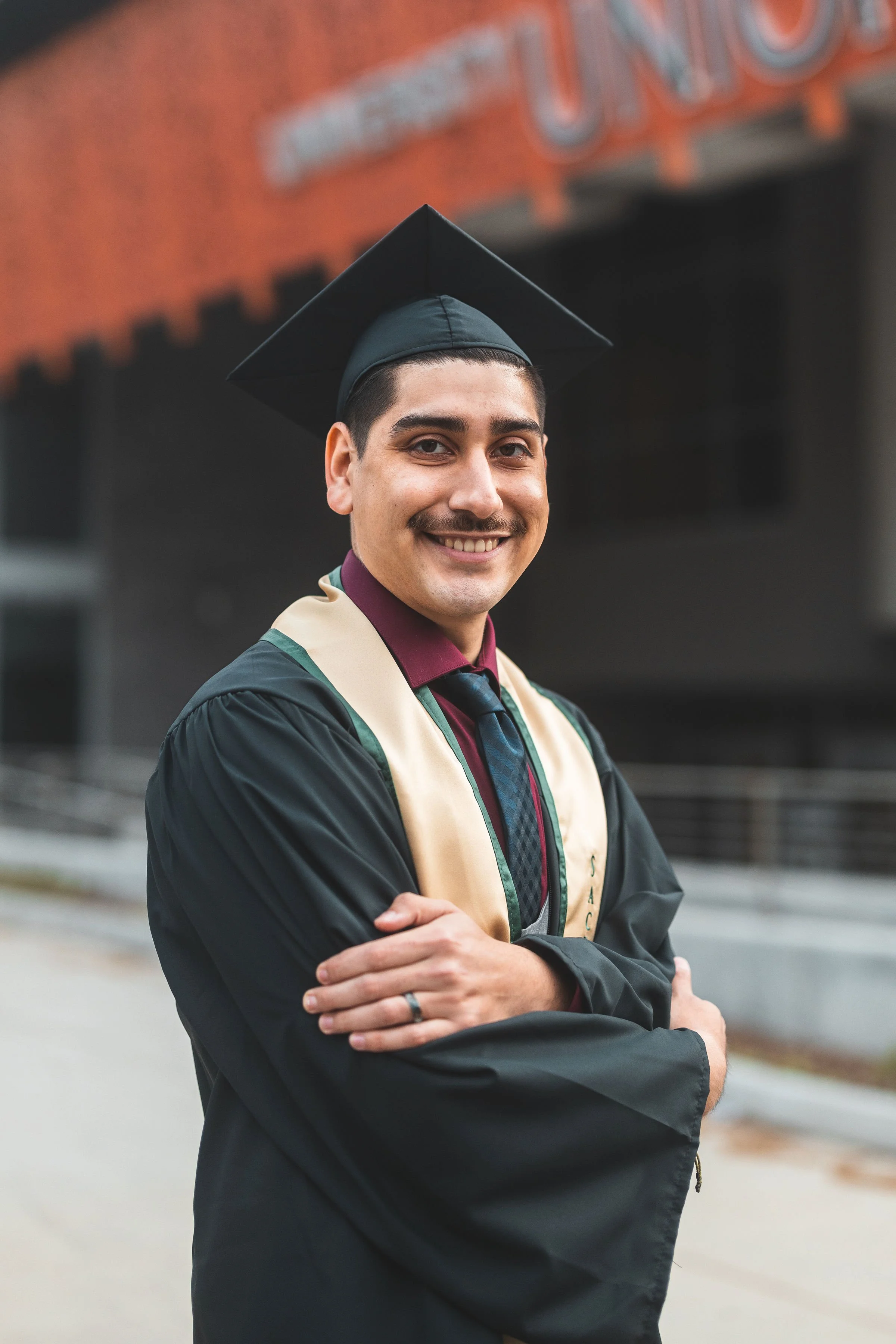 Young man in graduation cap and gown smiling outdoors.