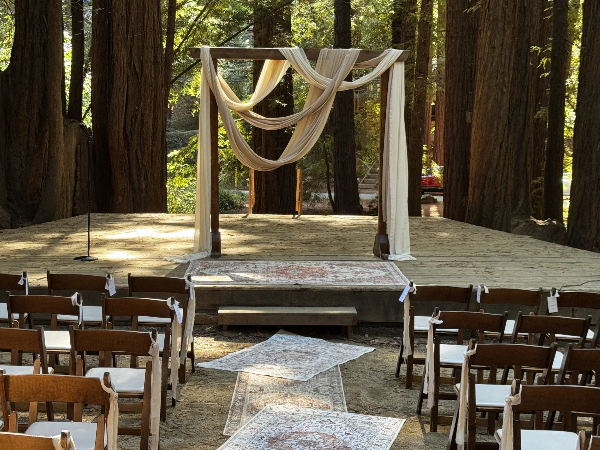Two large floral arrangements with pink roses, purple orchids, and peach dahlias on a white tablecloth against a wallpapered background with a scenic pastoral pattern.