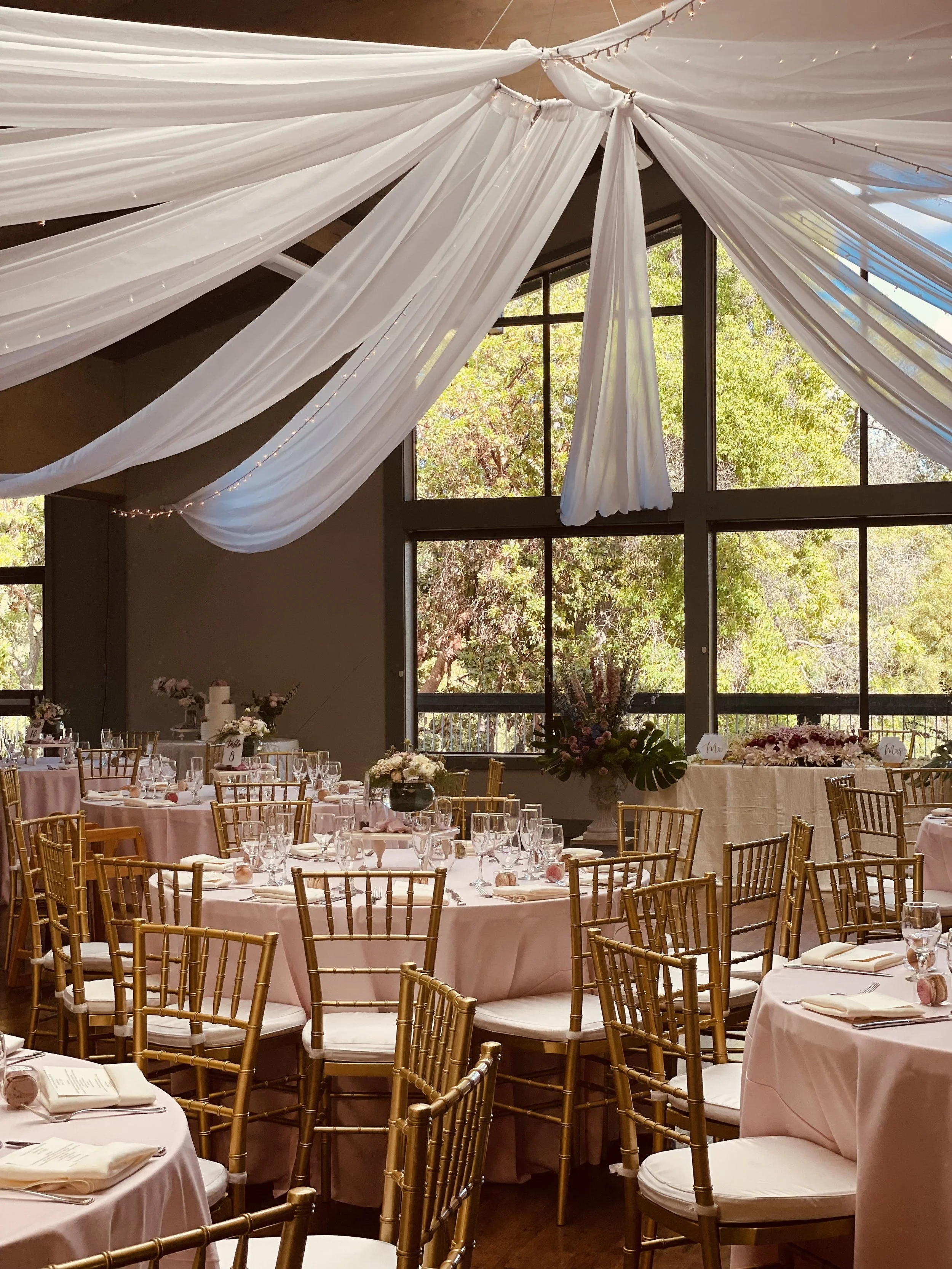 A three-tiered wedding cake with an edible topper of a bride and groom dancing, decorated with pink and white icing, roses, pearls, and horseshoes.