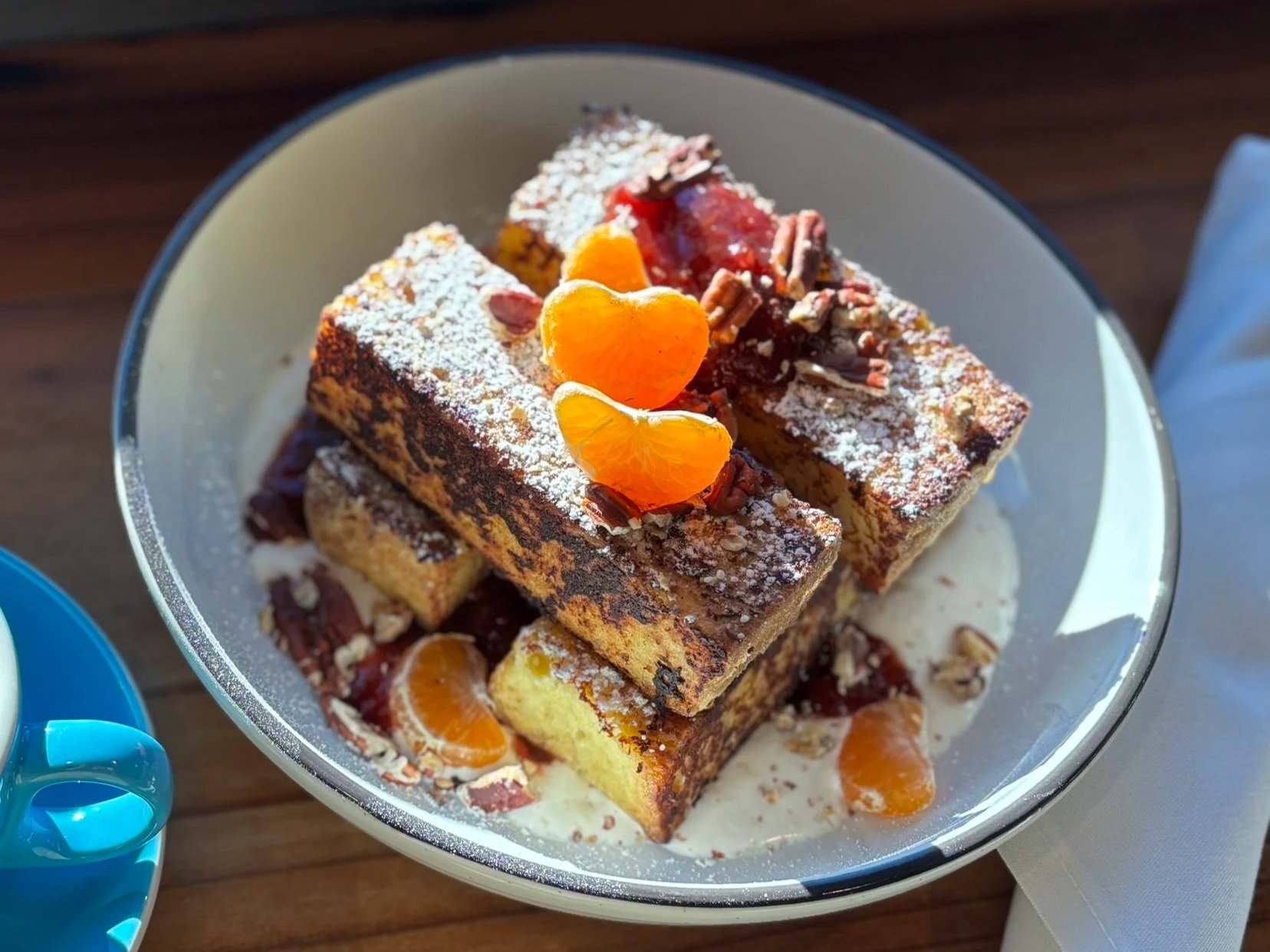 Stack of three dessert bars topped with powdered sugar, orange slices, and nuts on a silver plate.