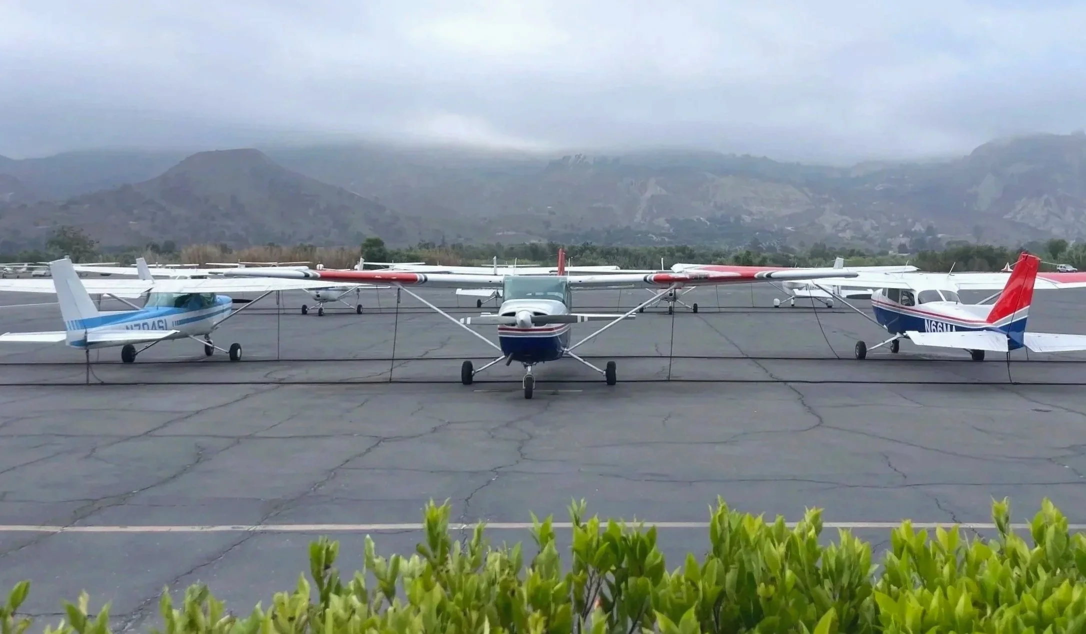 Three small planes parked on a cracked asphalt tarmac with mountains in the background and cloudy sky.