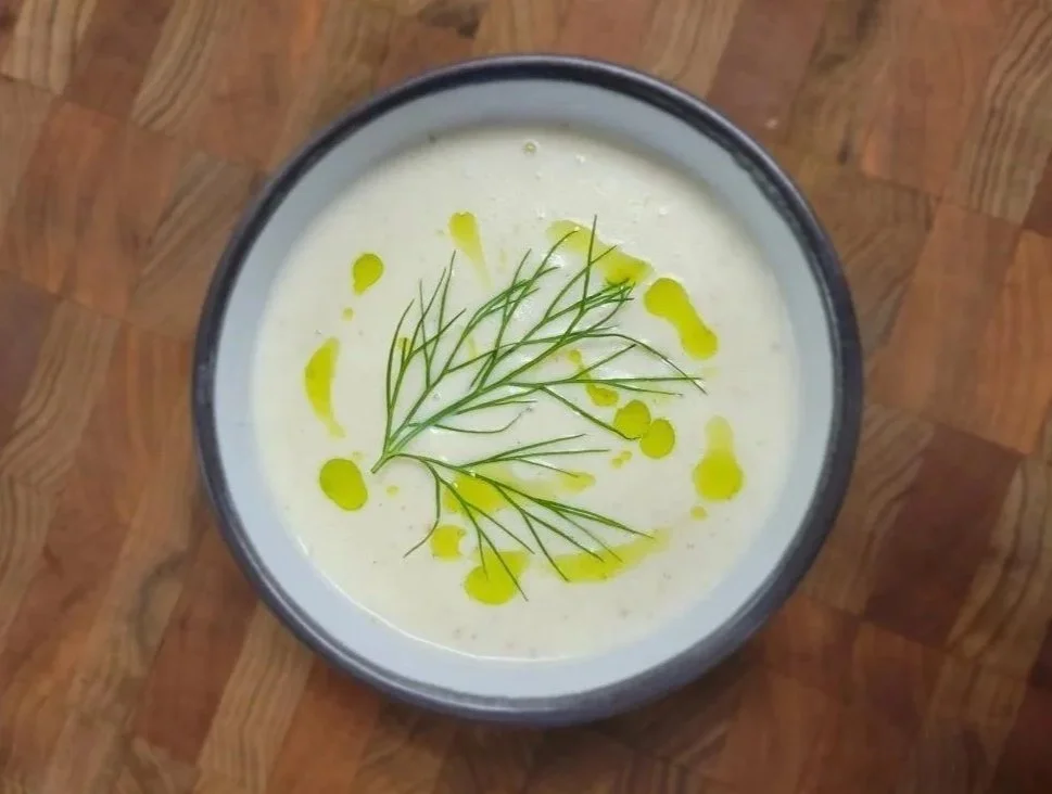 Bowl of creamy soup garnished with dill and drizzled with olive oil, on a wooden surface.