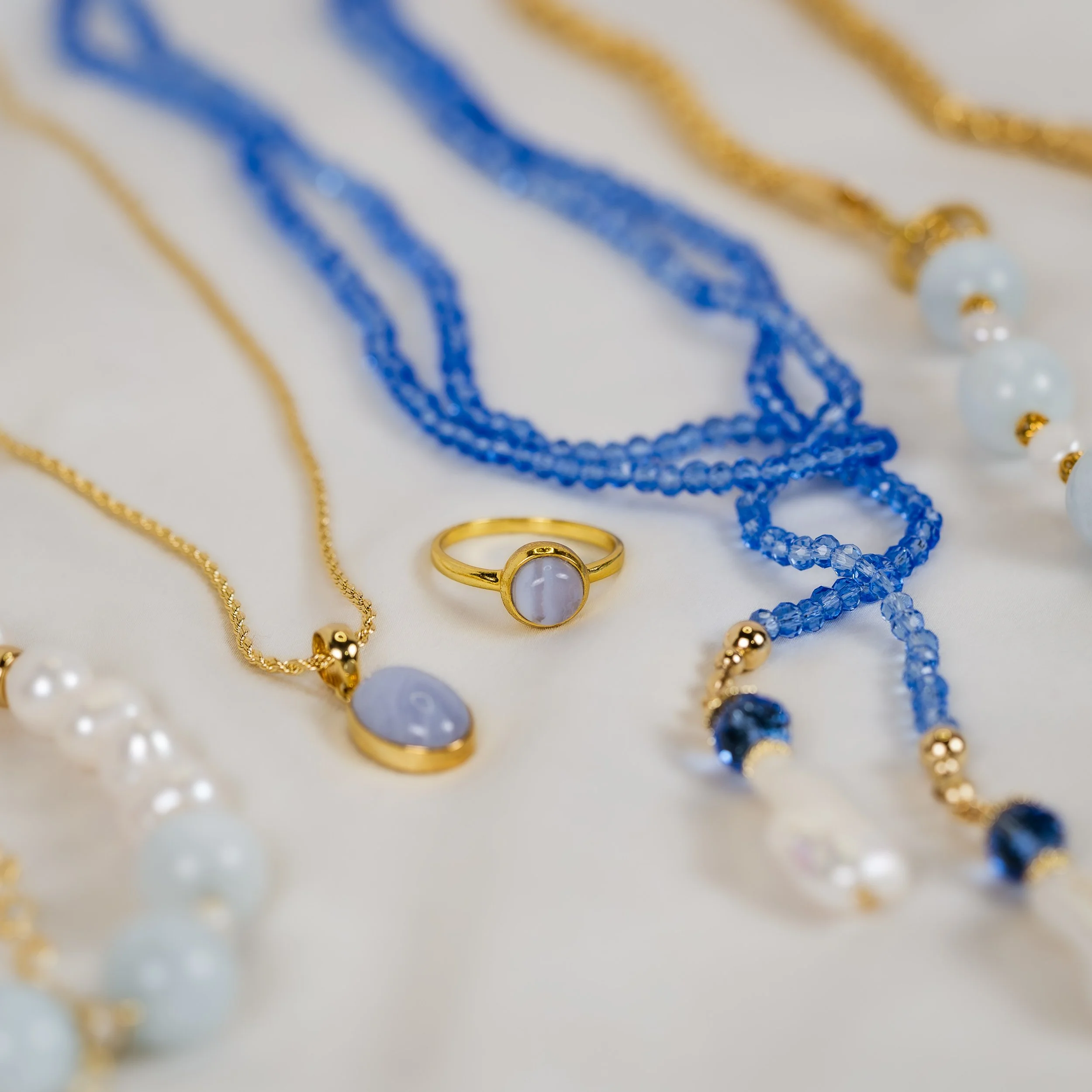 Gold and blue jewelry including necklaces and rings on a white surface.