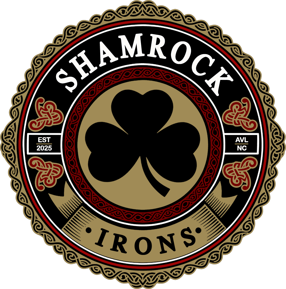 A circular logo with a black background and a gold shamrock in the center. The text "SHAMROCK IRONS" is at the top and "EST 2025" is on the left side, with "AVL NC" on the right side. The design is adorned with red and gold Celtic knot patterns.