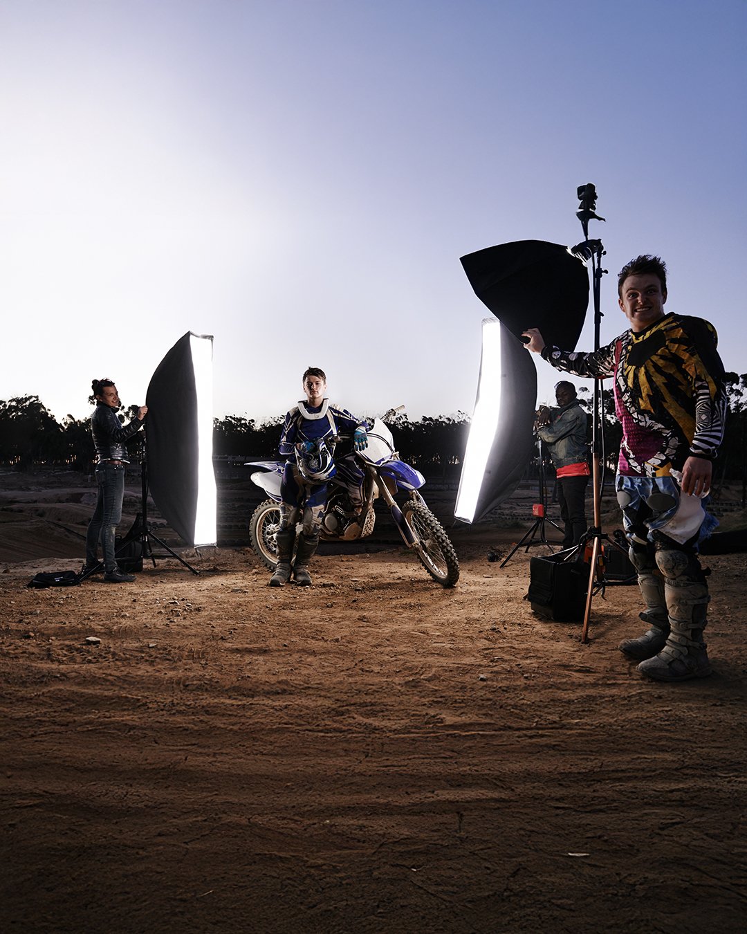 Equipo de fotografía profesional mezclándose con motociclistas en una sesión al aire libre al atardecer, con iluminación de estudio y un fondo natural.