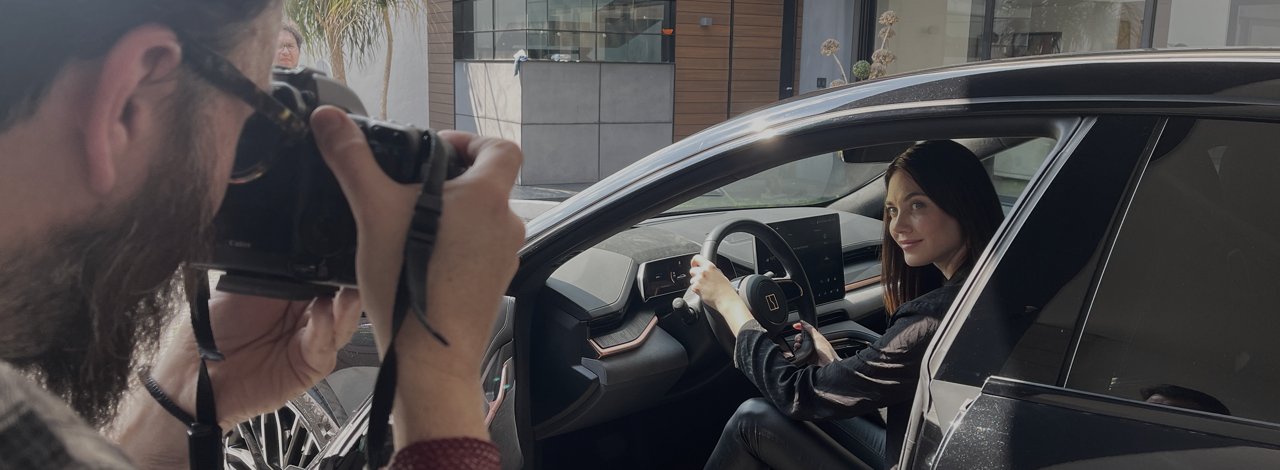 Una mujer conduciendo un automóvil y un fotógrafo capturando la imagen desde afuera del vehículo.
