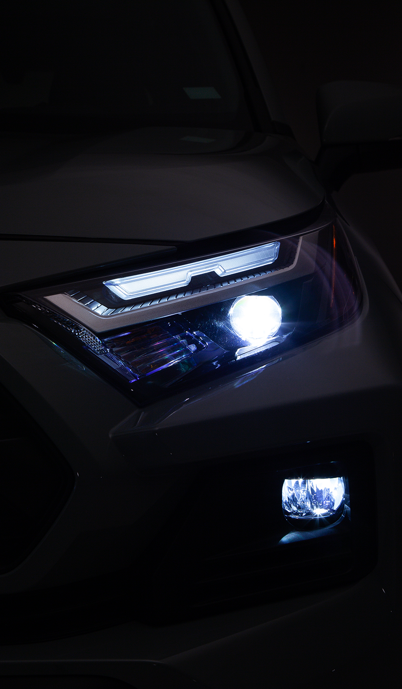 Primer plano de los faros delanteros de un automóvil oscuro con luces encendidas, en un entorno oscuro.