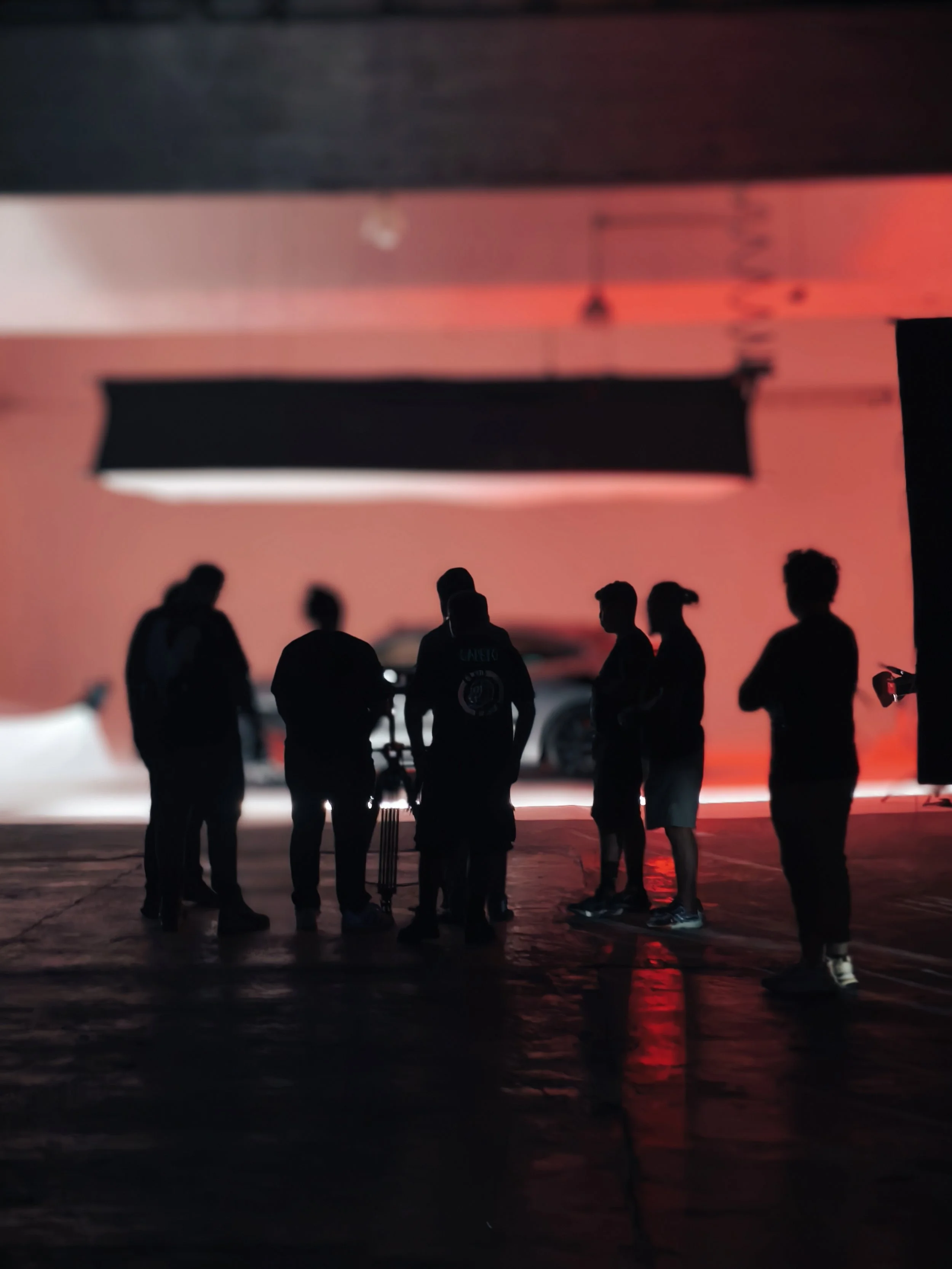 Grupo de personas en una sala con iluminación roja y negra, algunas con cámaras y equipo de grabación, en lo que parece ser una sesión de grabación o filmación.