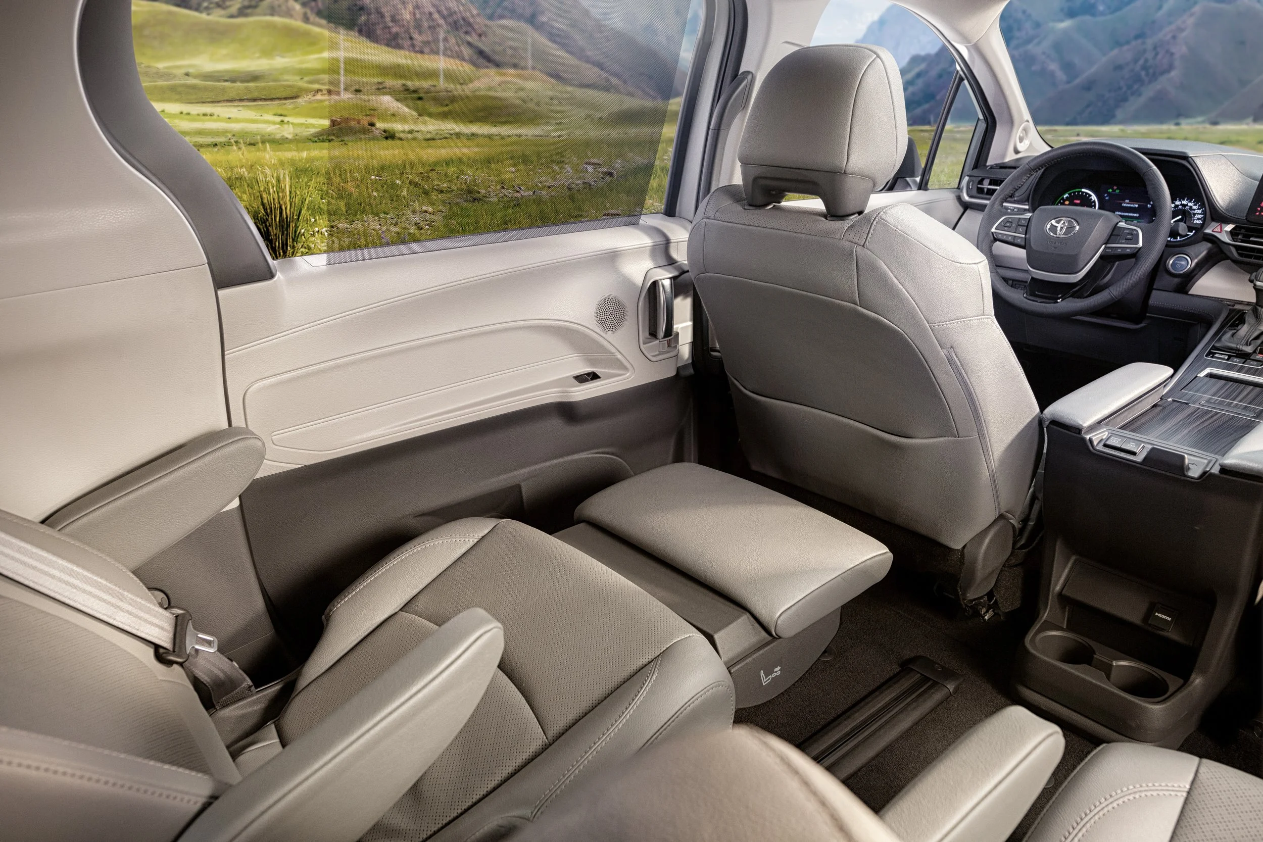 Interior de una camioneta con asientos de color gris, tablero de instrumentos y volante visible, y una ventana mostrando un paisaje de montañas y praderas verdes.