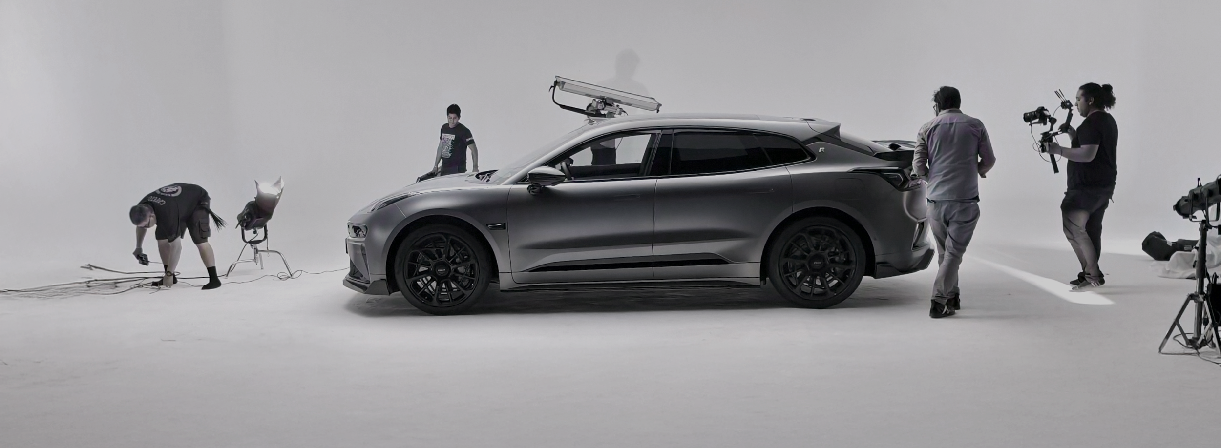 Equipo de producción filmando un automóvil negro en un estudio con fondo blanco.