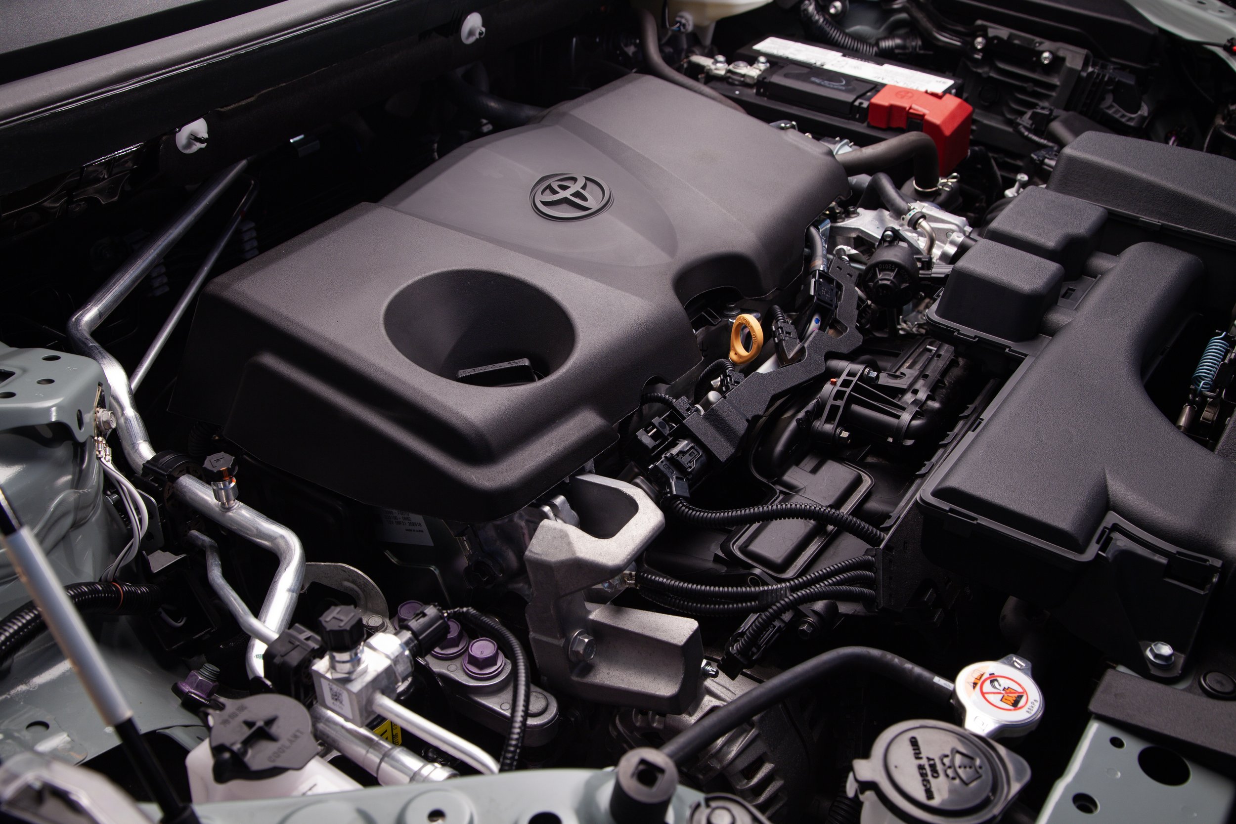 Motor de automóvil con componentes visibles, incluyendo maletero de fluidos, cables y piezas metálicas.