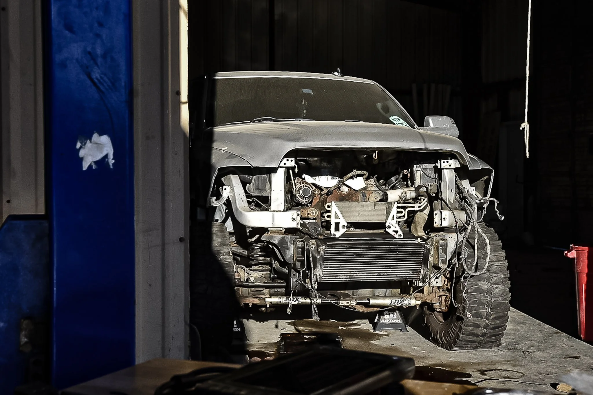 A partially disassembled off-road vehicle with exposed engine components inside a dimly lit garage.