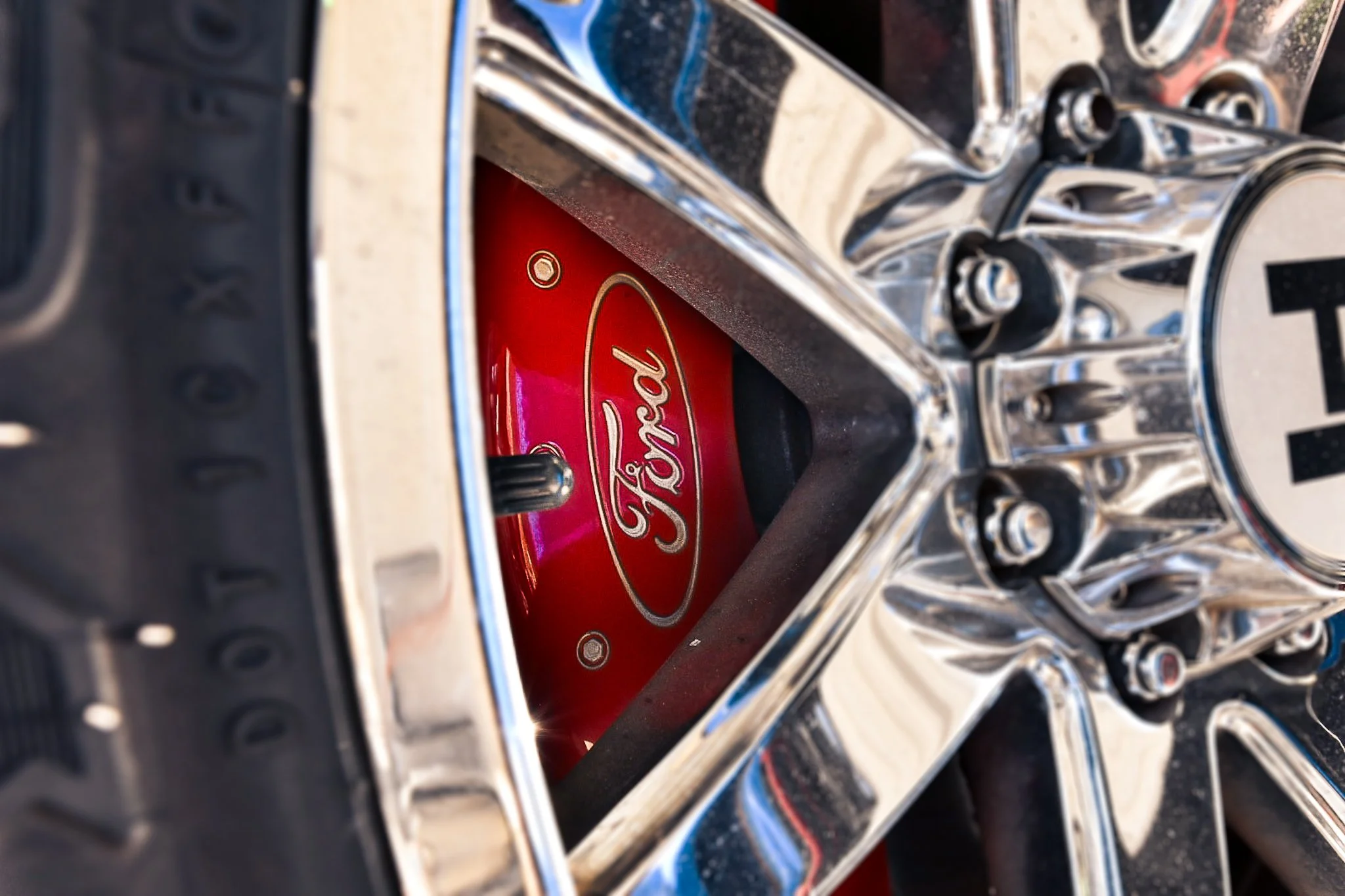Close-up of a chrome wheel of a Ford vehicle, with a red Ford hubcap visible through the center.