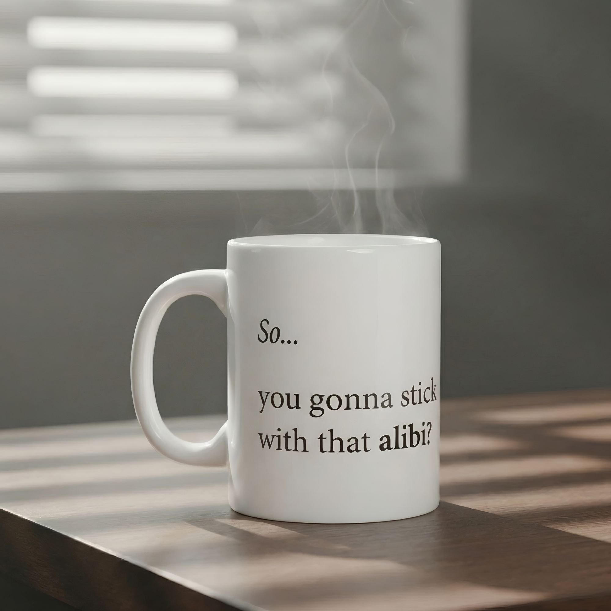 The Alibi Mug 11oz white ceramic - resting on a dark wood table with soft light filtering through window bliinds