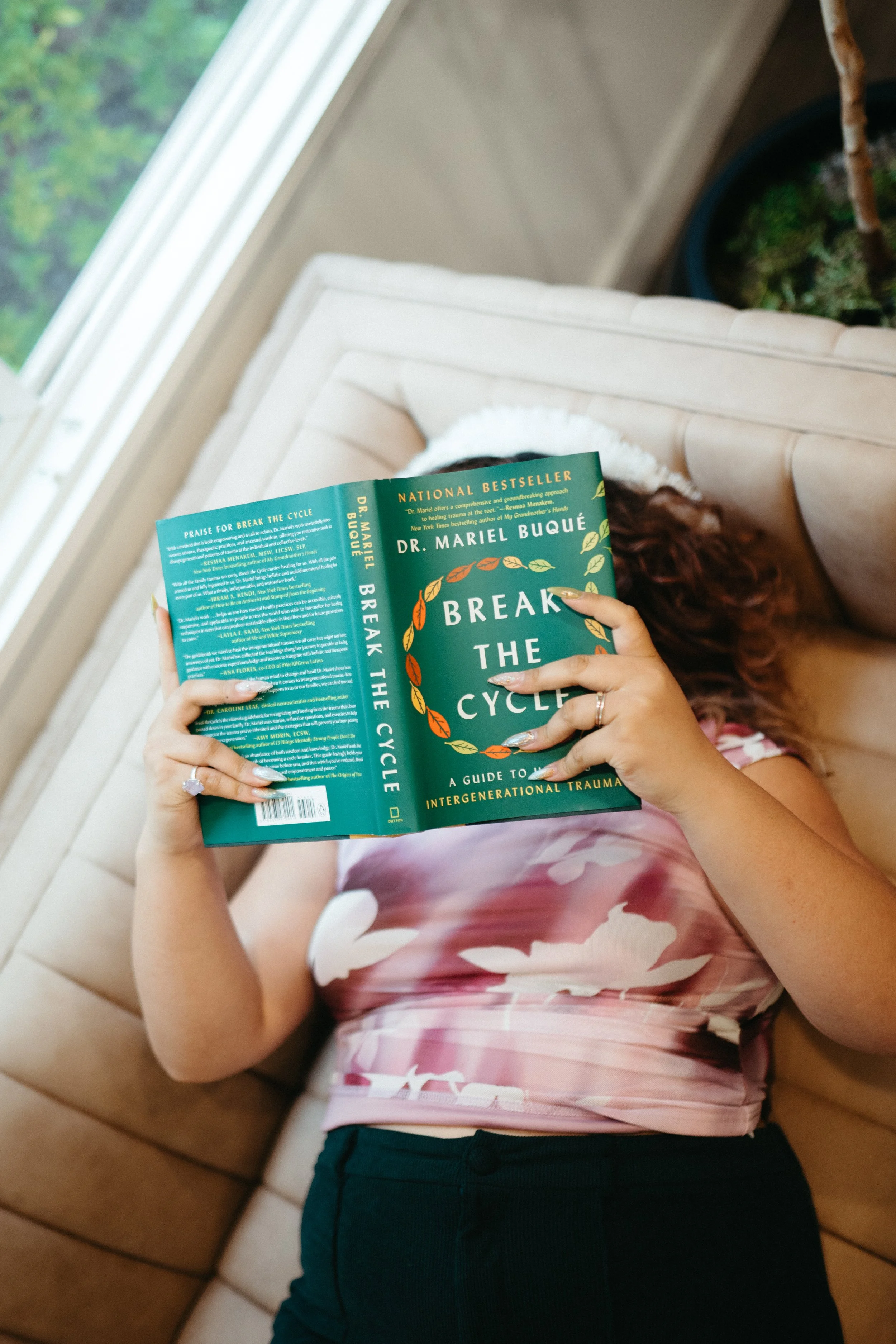 Photo of a person lying on a couch reading holding a book called Break the Cycle above them